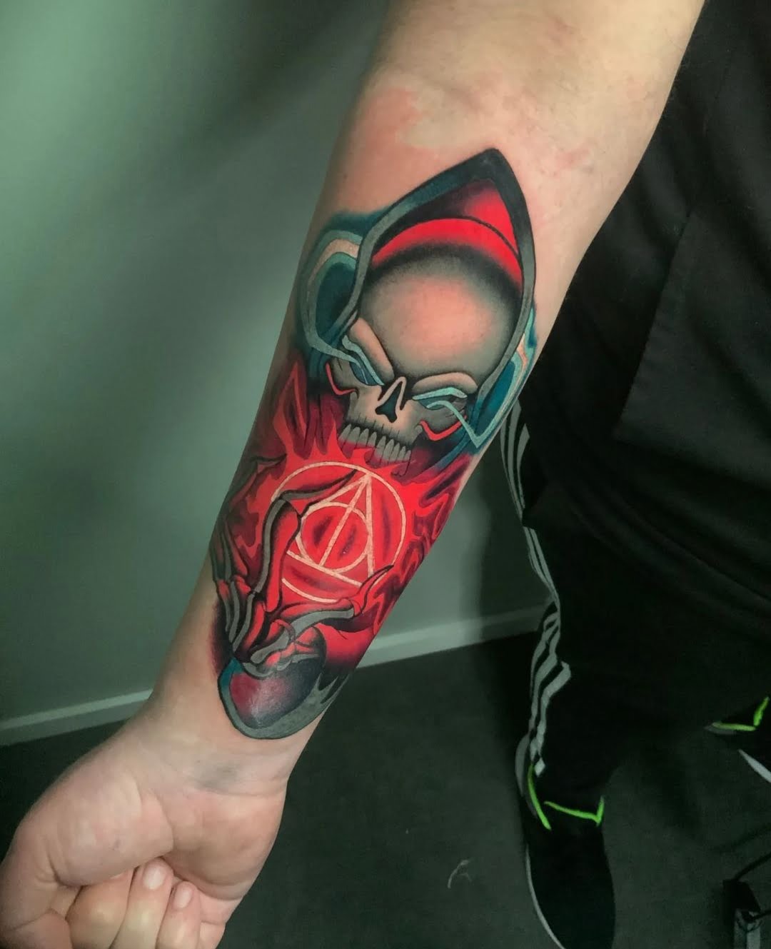 Tatuaje de calavera en estilo neotradicional con tonos rojos y azules en el antebrazo