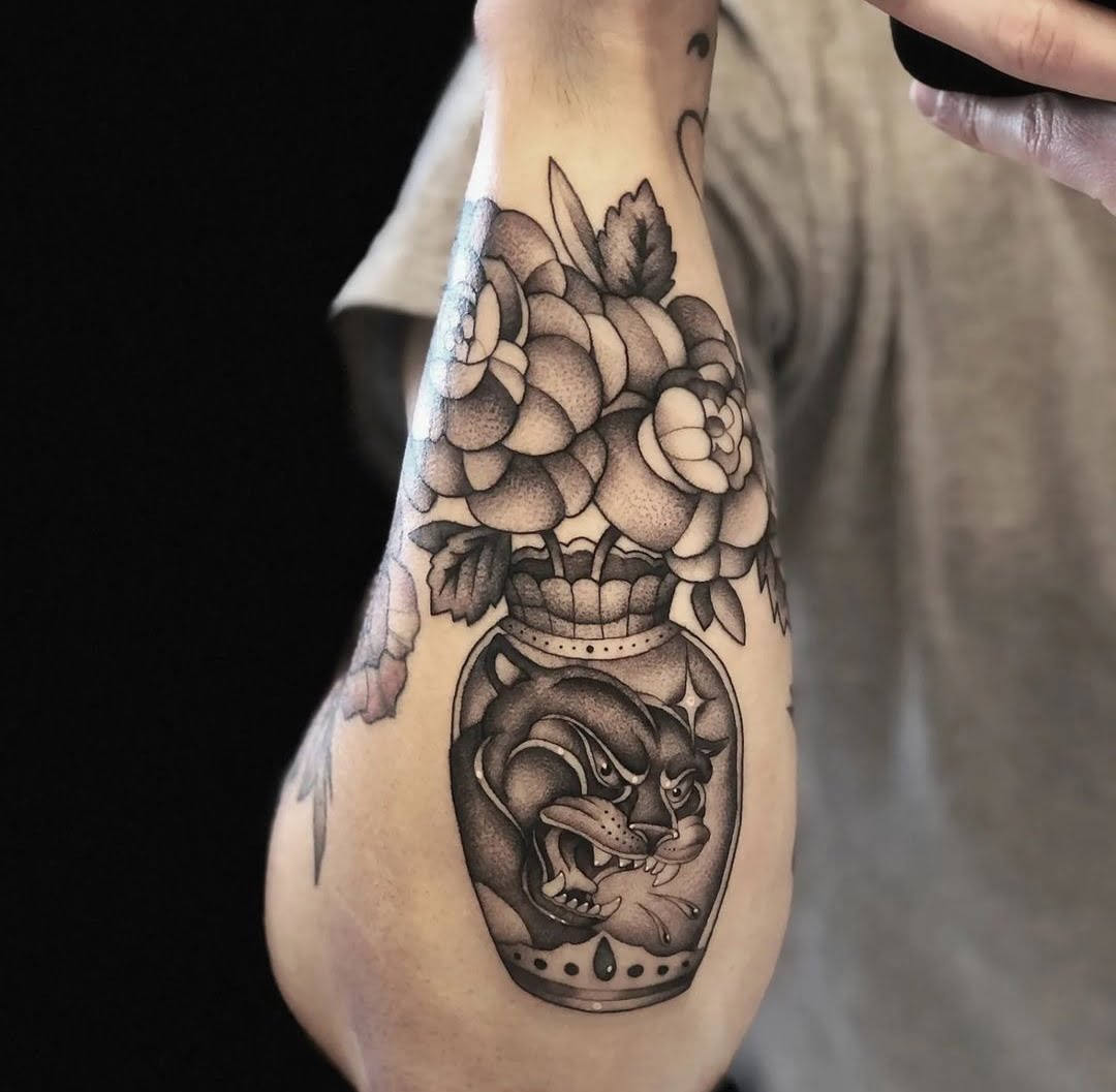 Tatuaje blackwork de un florero con flores y una pantera en el antebrazo, destacando un sombreado detallado y contraste en blanco y negro.