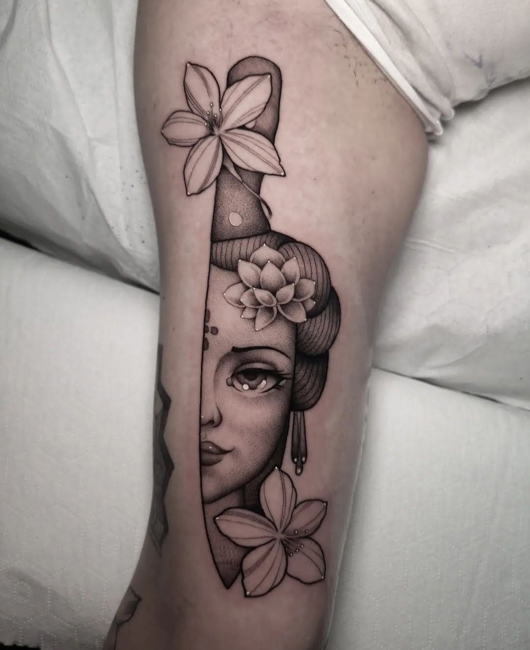 Tatuaje de geisha en estilo blackwork con flores en la pierna, transmitiendo elegancia y serenidad.