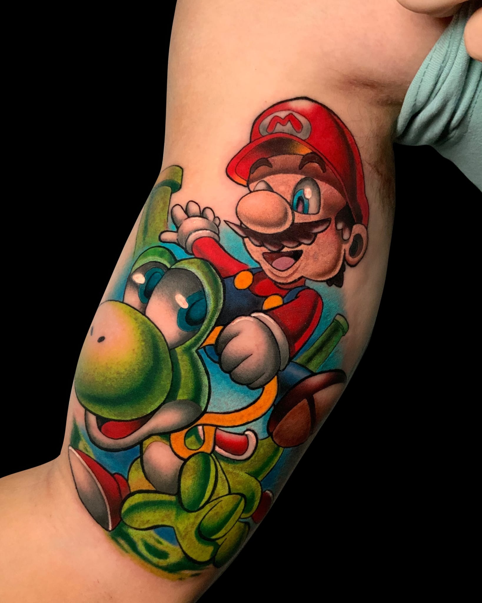 Tatuaje colorido de Mario montando a Yoshi en estilo neotradicional en el bíceps.
