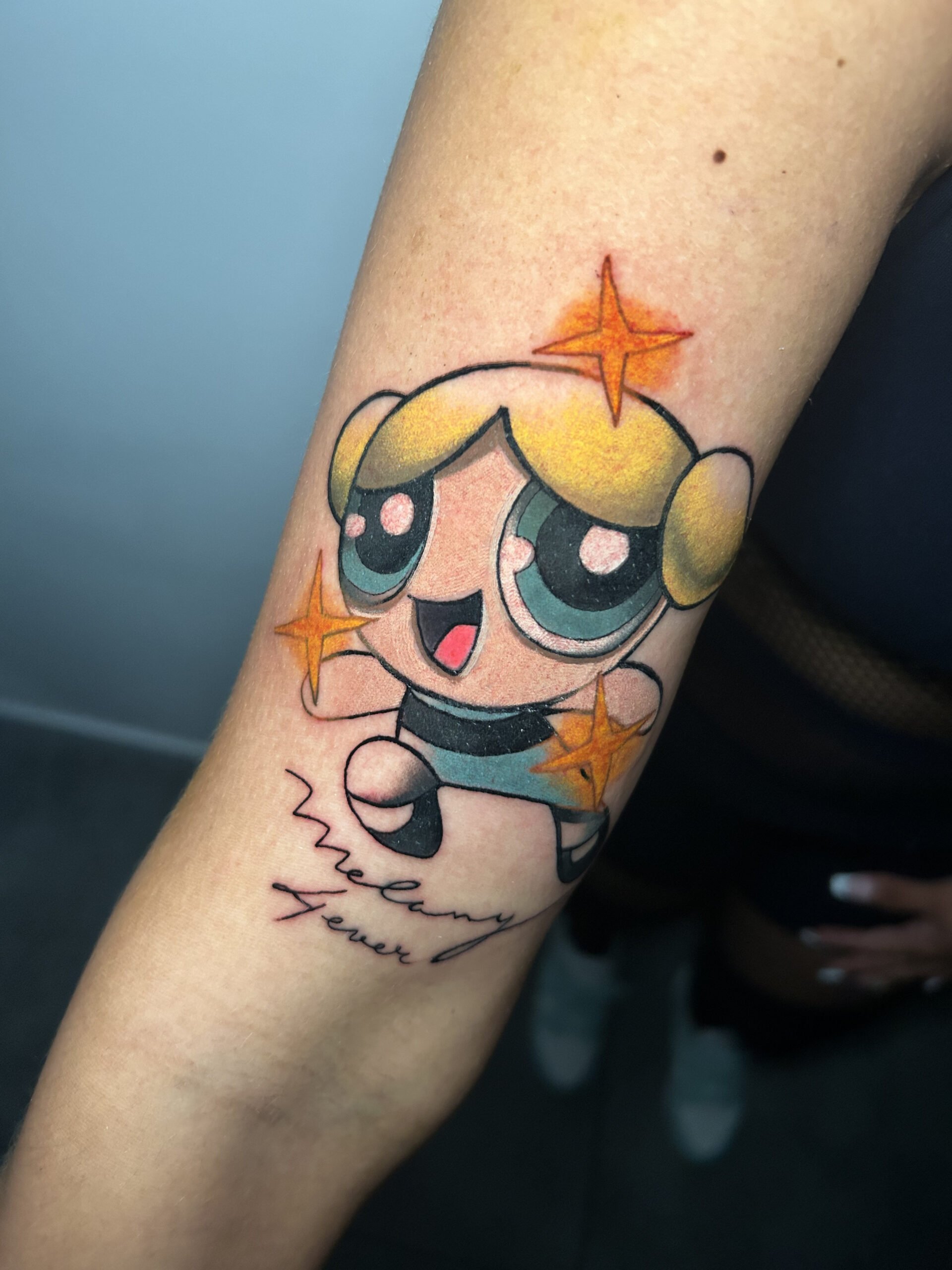 Tatuaje de personaje animado con técnica fineline y colores vibrantes en el antebrazo transmitiendo alegría.