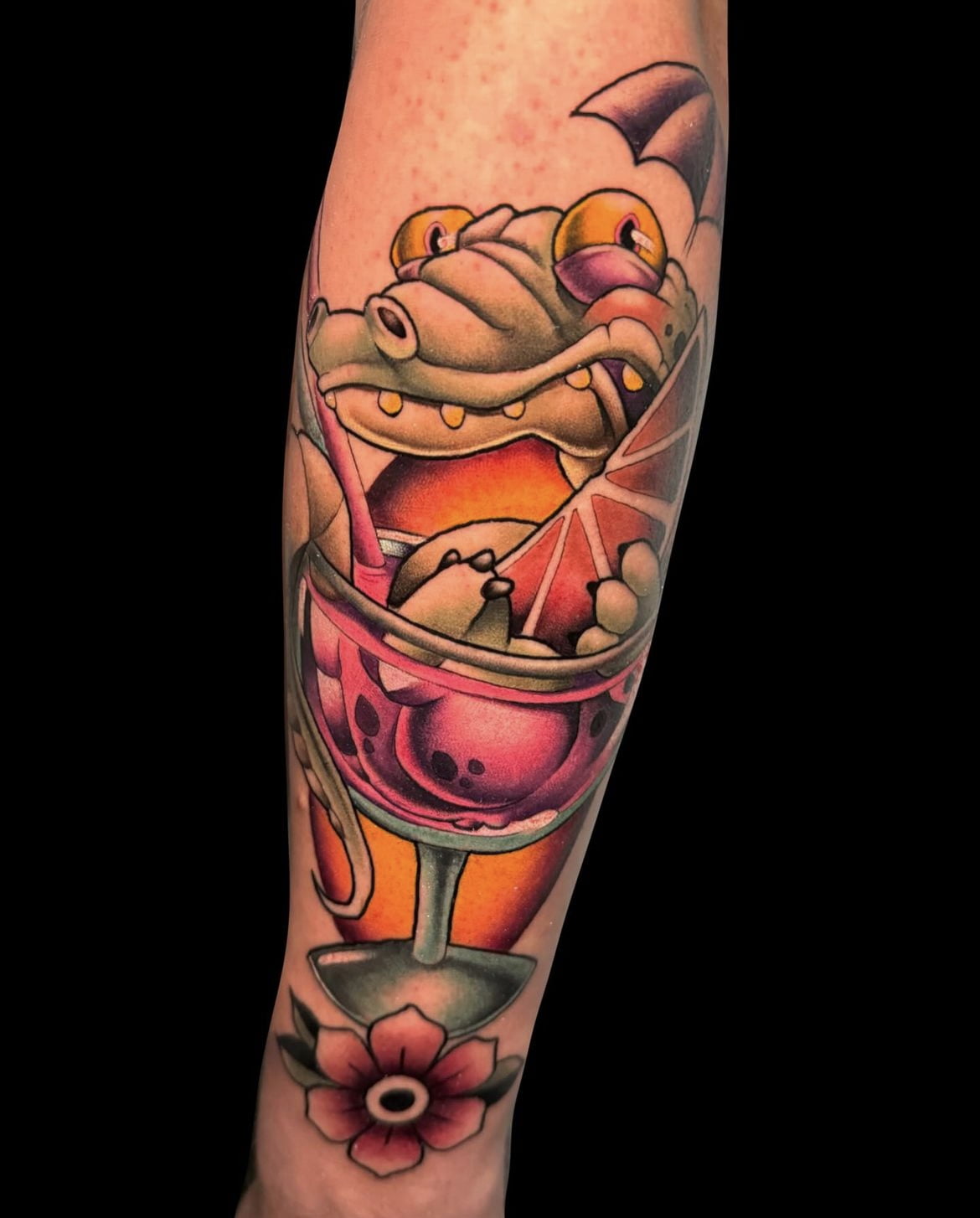 Tatuaje de cocodrilo en copa de cóctel, estilo neotradicional en pierna, colores vibrantes.