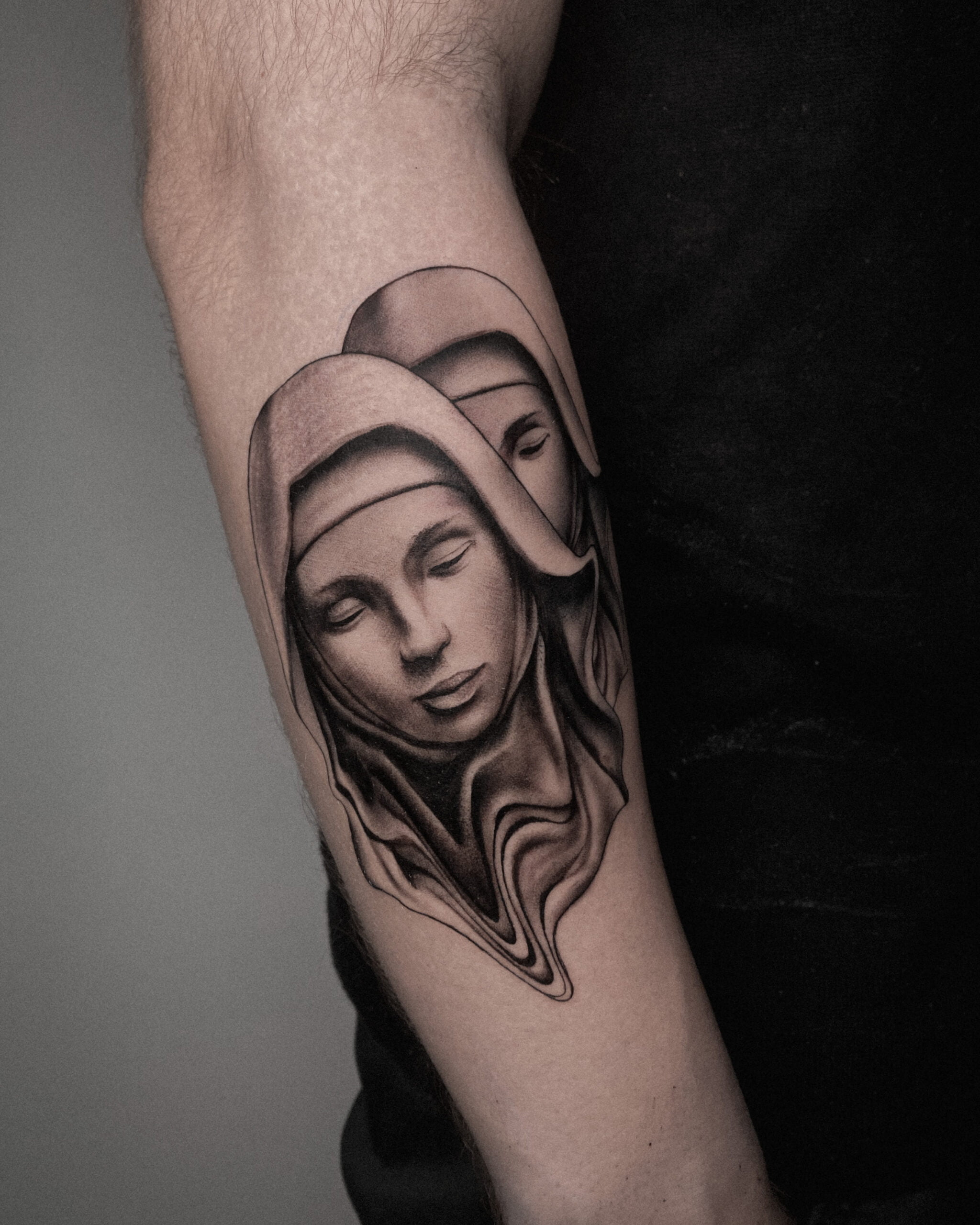 Tatuaje de dos figuras religiosas en estilo realista y black and grey en el antebrazo, transmitiendo serenidad.
