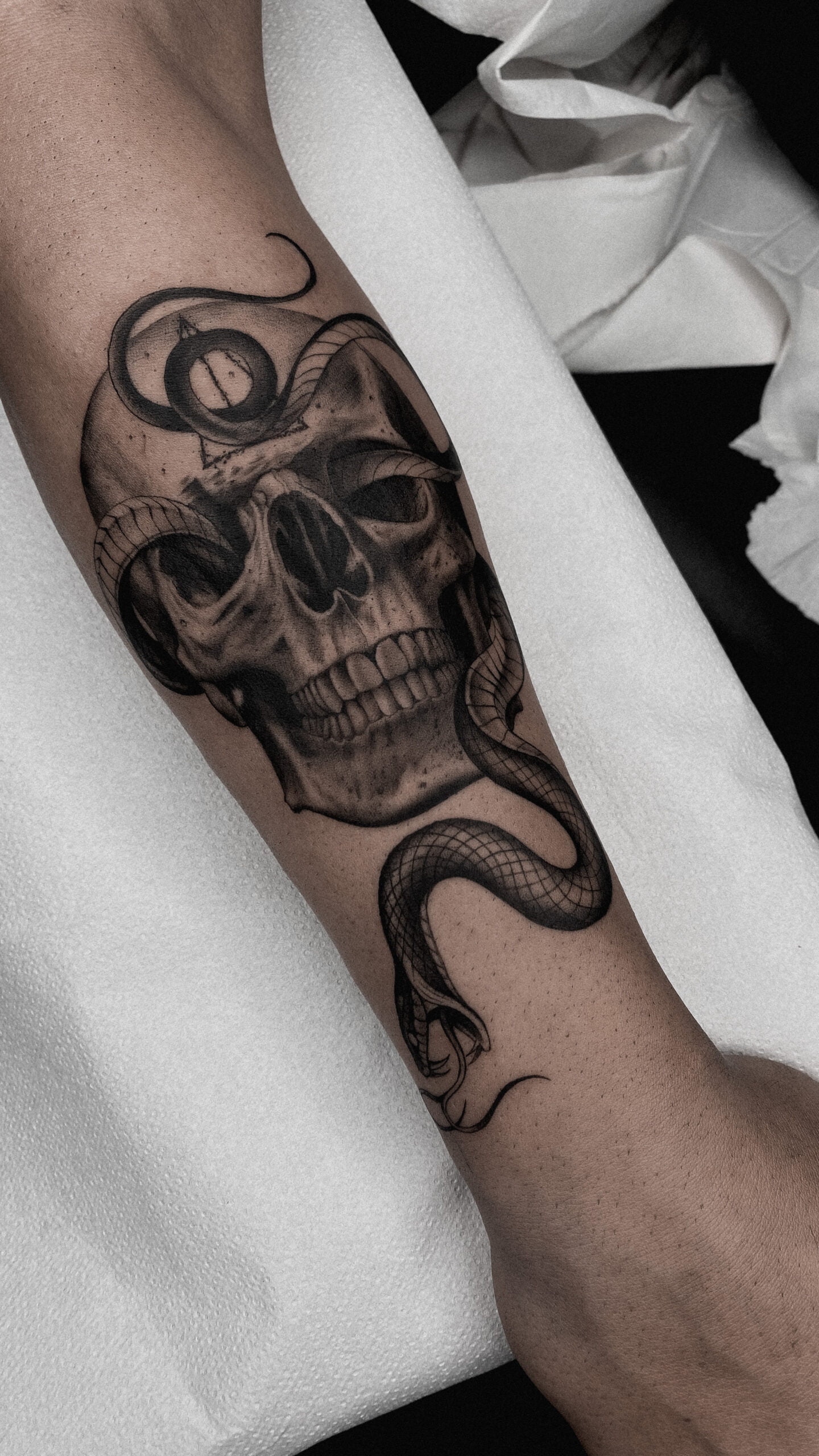 Tatuaje de calavera con serpiente en estilo realista black and grey en el brazo, transmitiendo una sensación de misterio y oscuridad.
