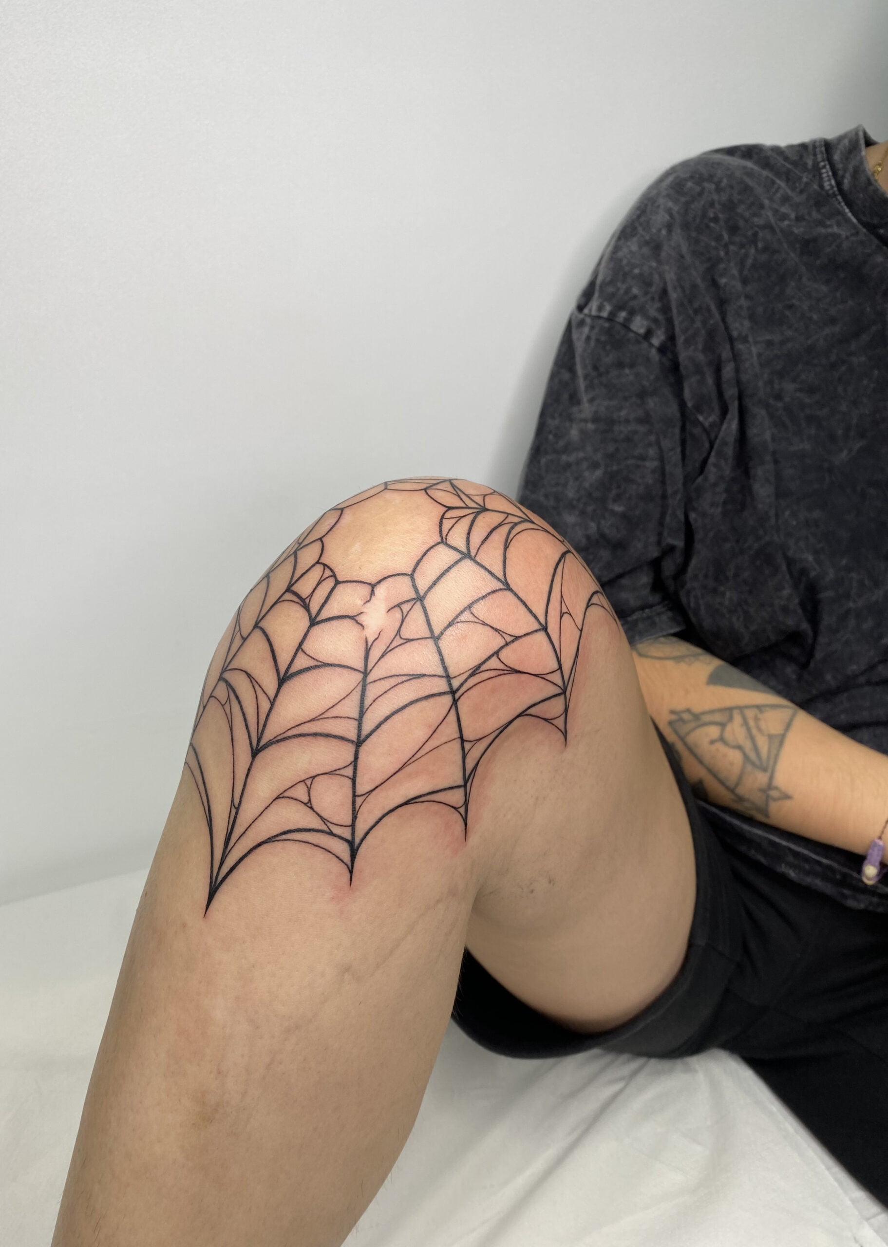 Tatuaje de telaraña en estilo blackwork realizado en la rodilla, transmitiendo un aire de misterio y conexión.