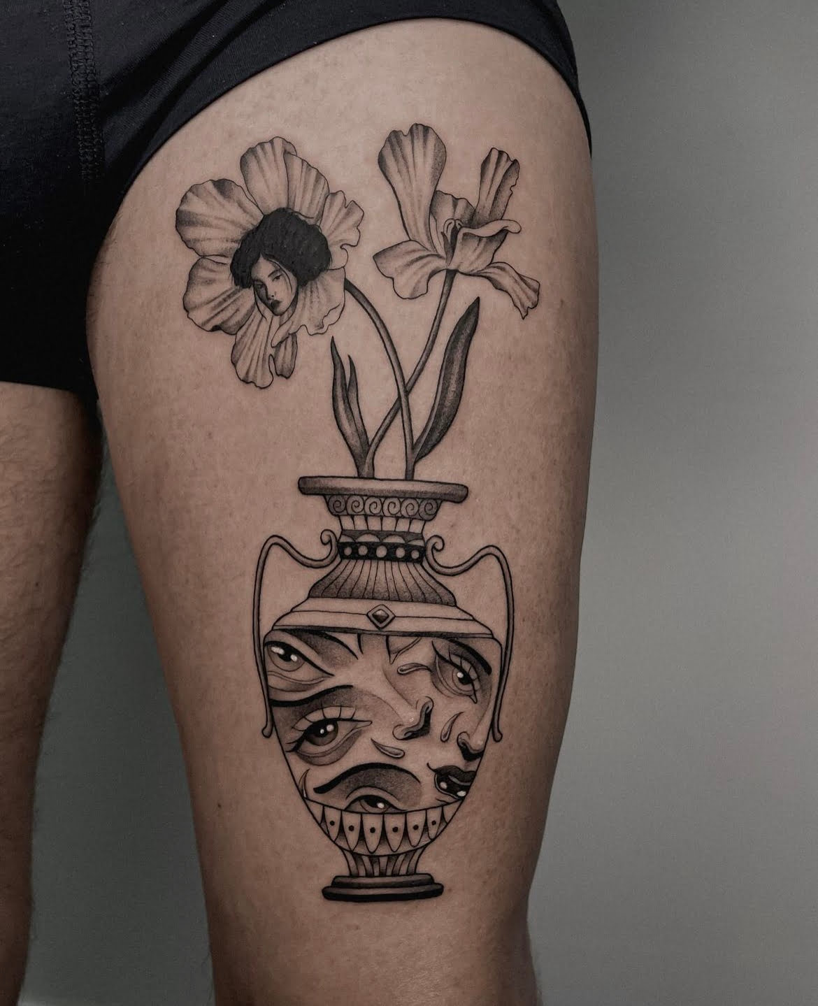 Tatuaje surrealista de jarrón con rostros e iris sombrados en estilo black and grey, en el muslo.