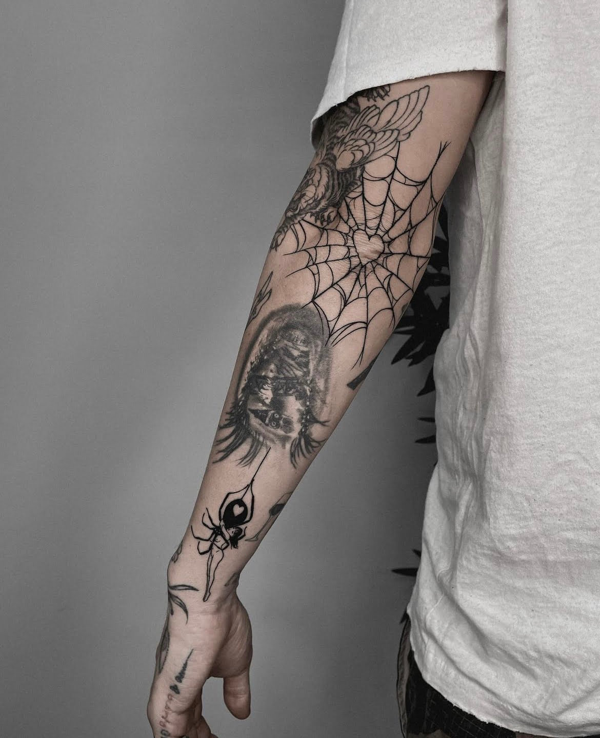 Tatuaje de telaraña en estilo blackwork en el antebrazo, con representación realista de una cara y una araña distintiva, transmitiendo misterio.