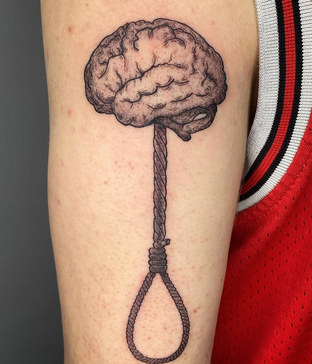 Tatuaje de cerebro con soga, estilo surrealista en el brazo, evocando reflexión.