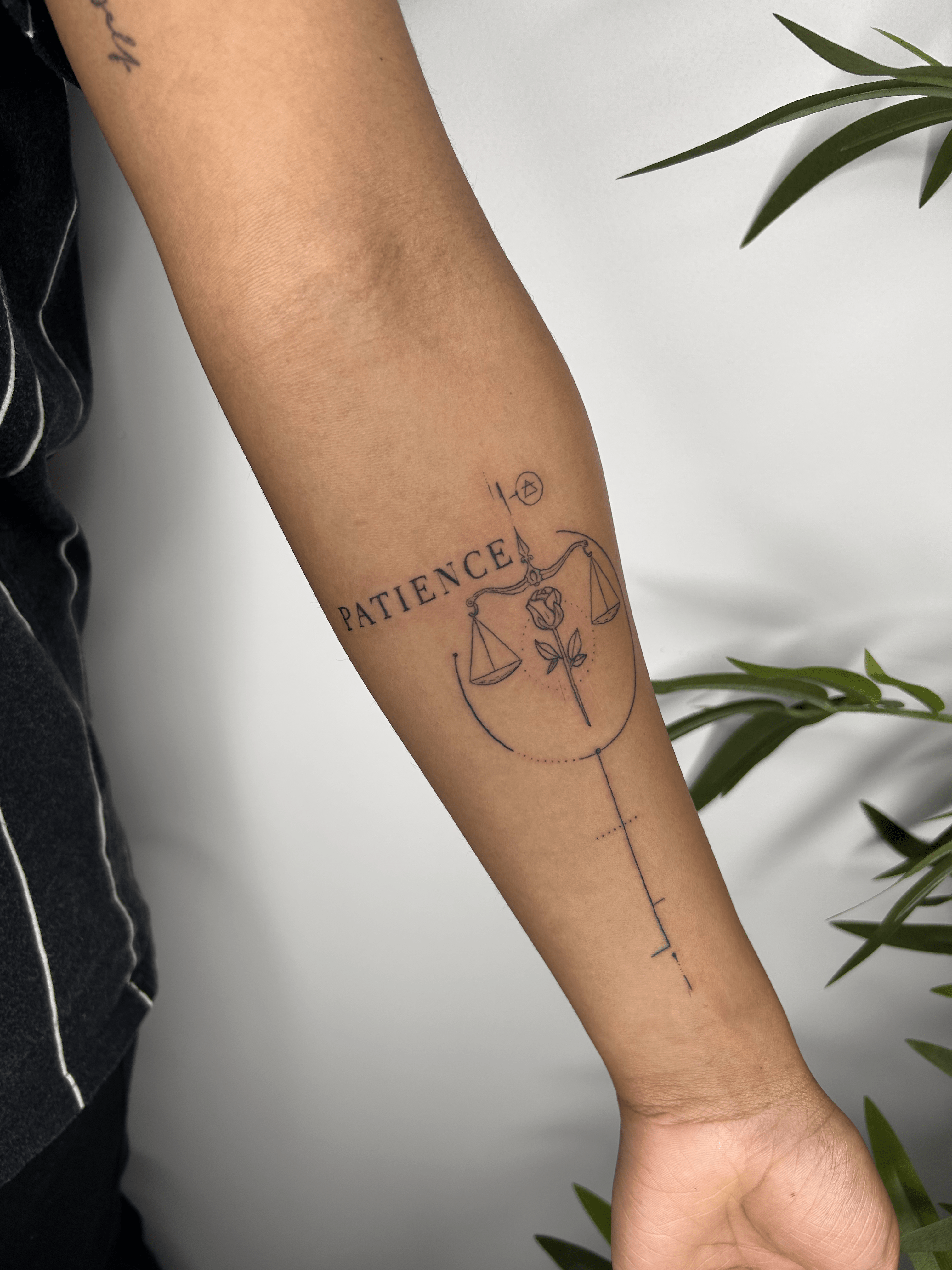Tatuaje de balanza con rosa en estilo fineline en el antebrazo, transmite equilibrio y paciencia.