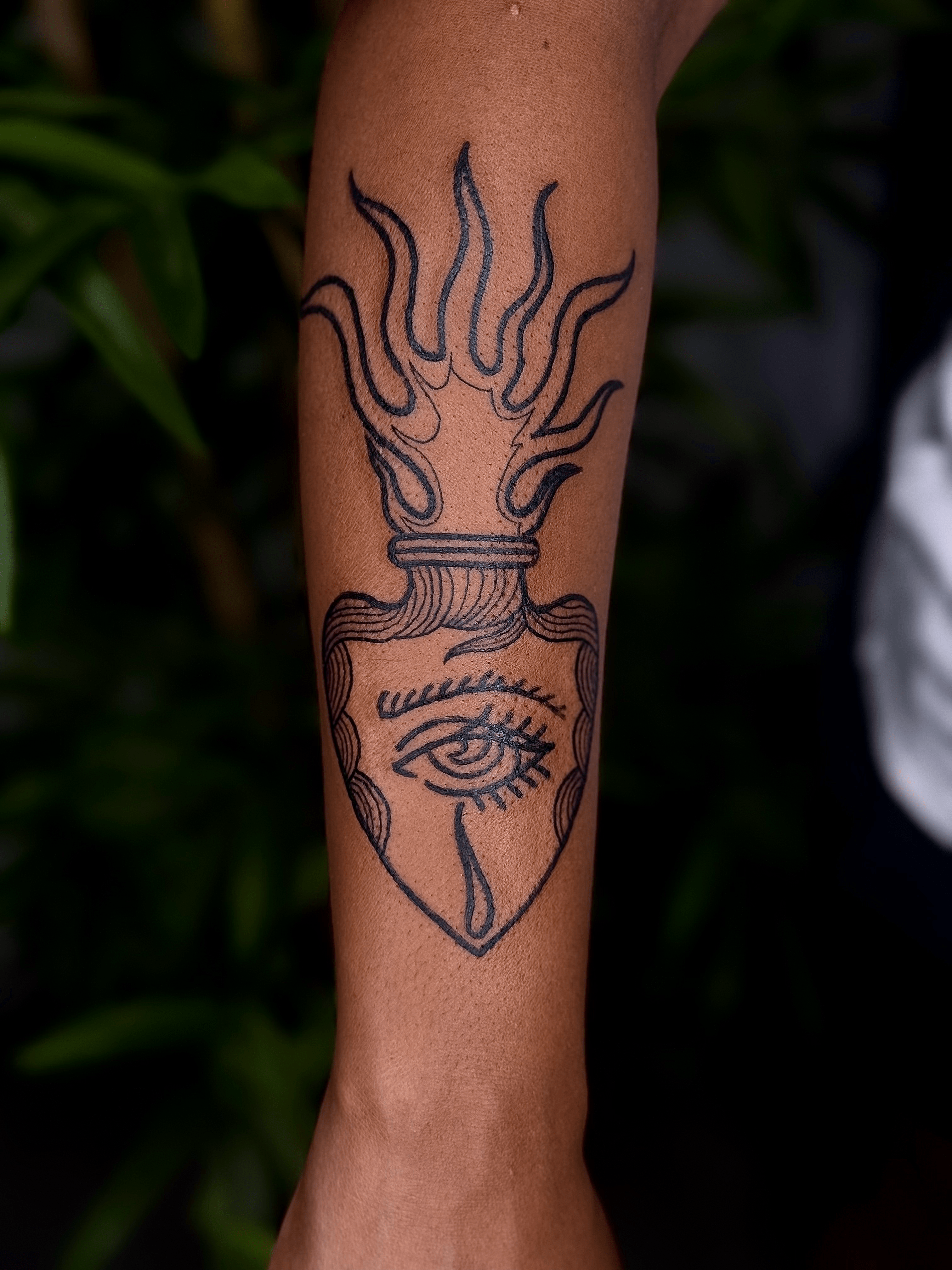 Tatuaje de un ojo estilizado con líneas simétricas en estilo blackwork en el antebrazo.