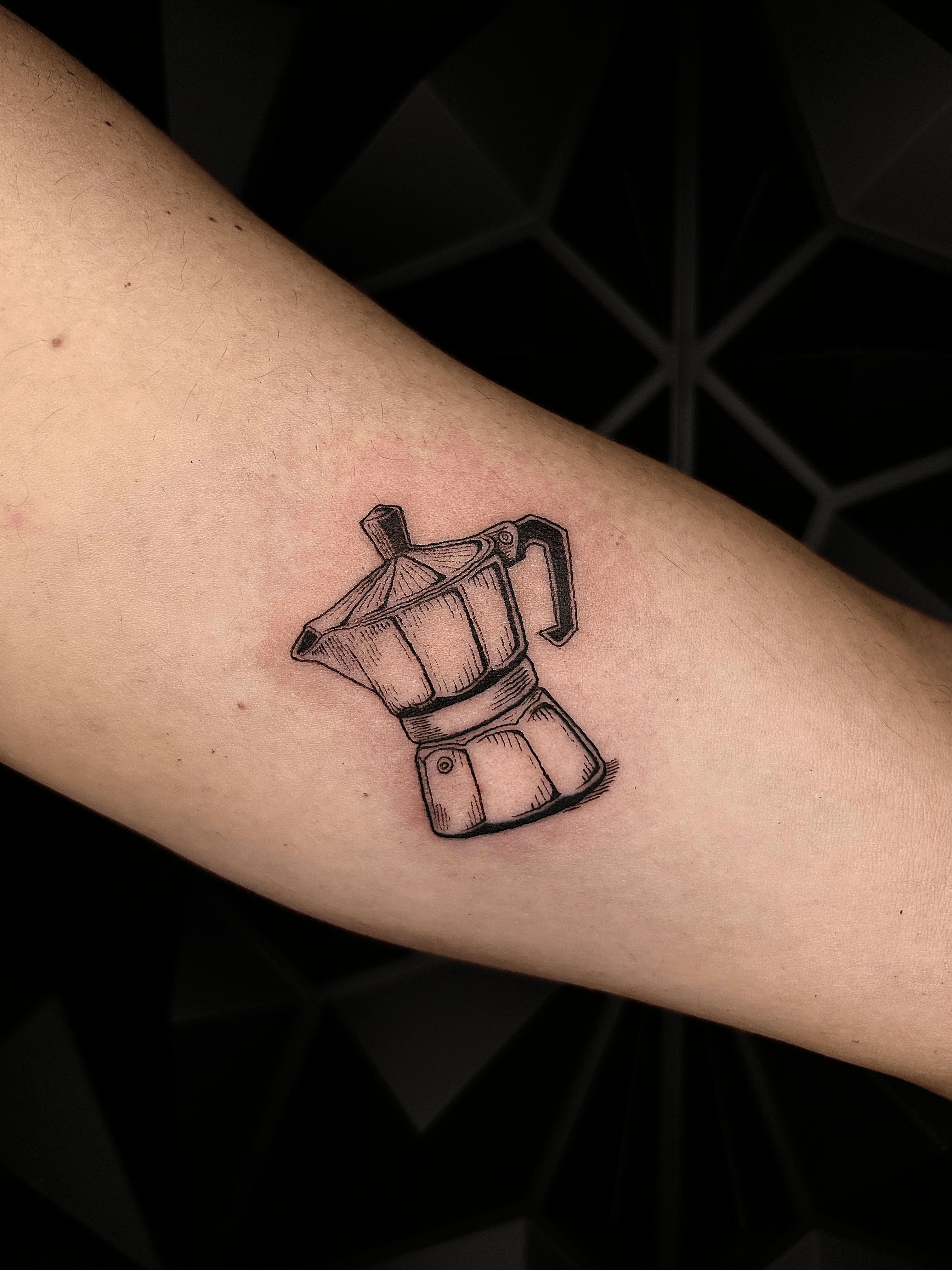 Tatuaje de cafetera Moka en estilo blackwork con líneas finas en el brazo.