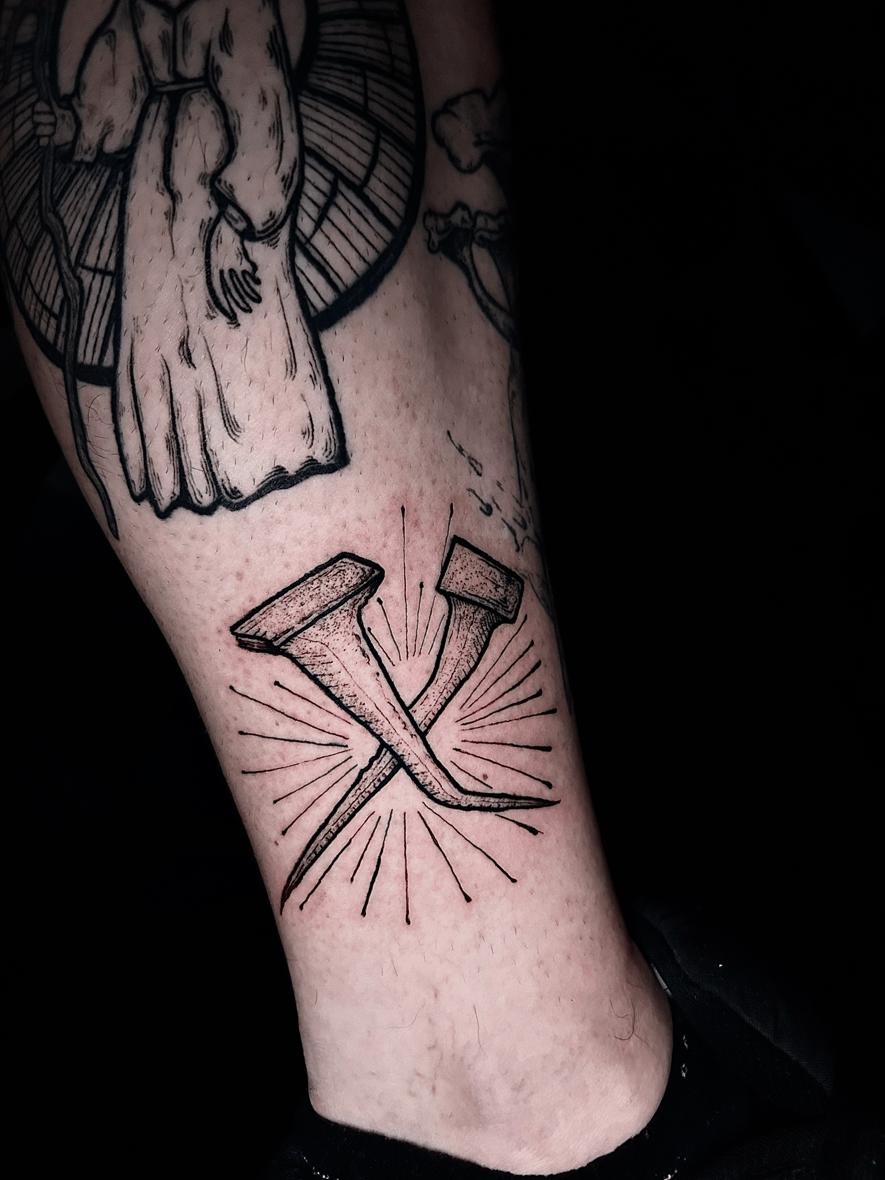 Tatuaje de clavos en estilo blackwork en la pantorrilla, transmitiendo fuerza.