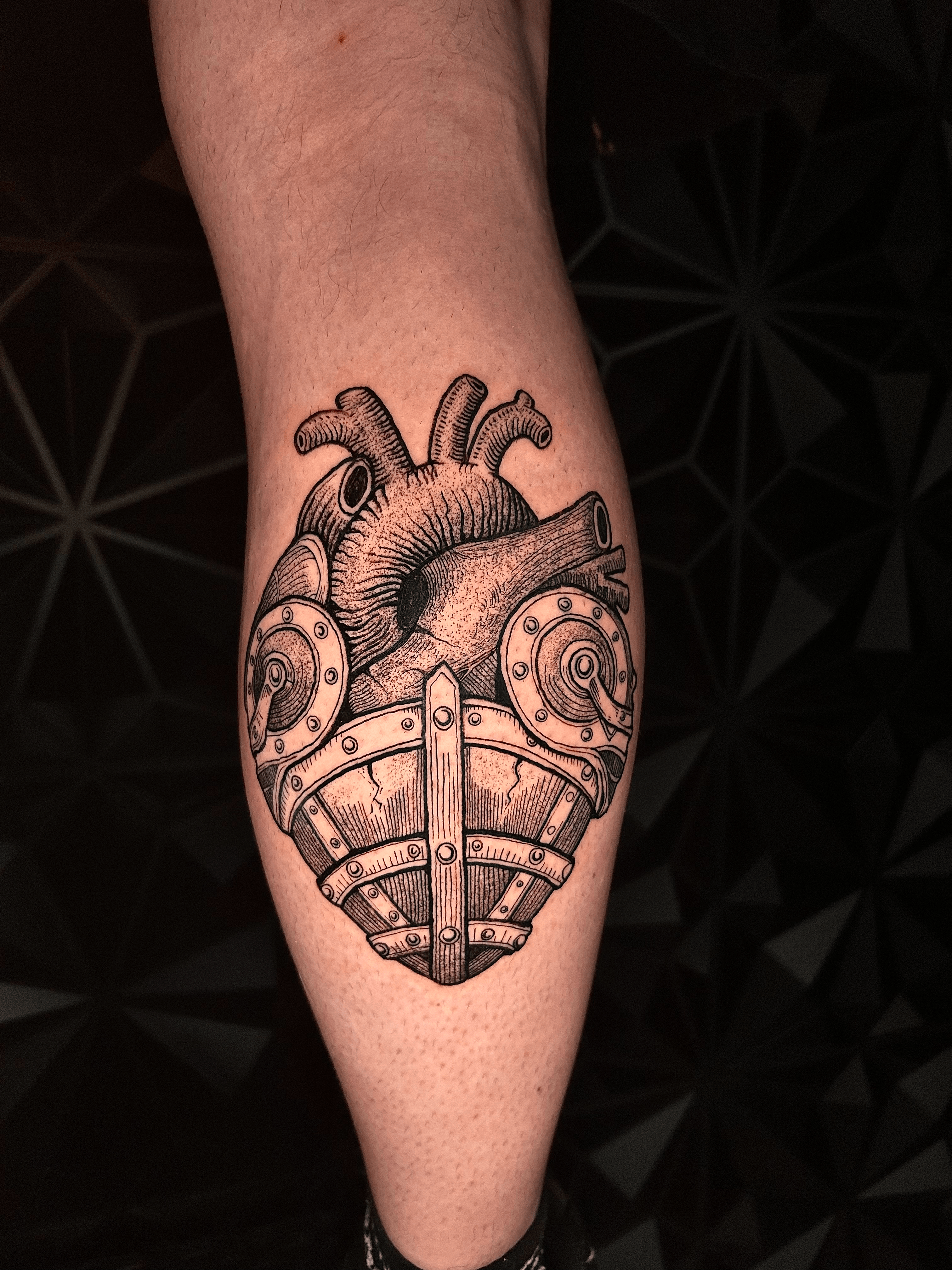 Tatuaje de un corazón anatómico blindado en estilo blackwork ubicado en la pierna.