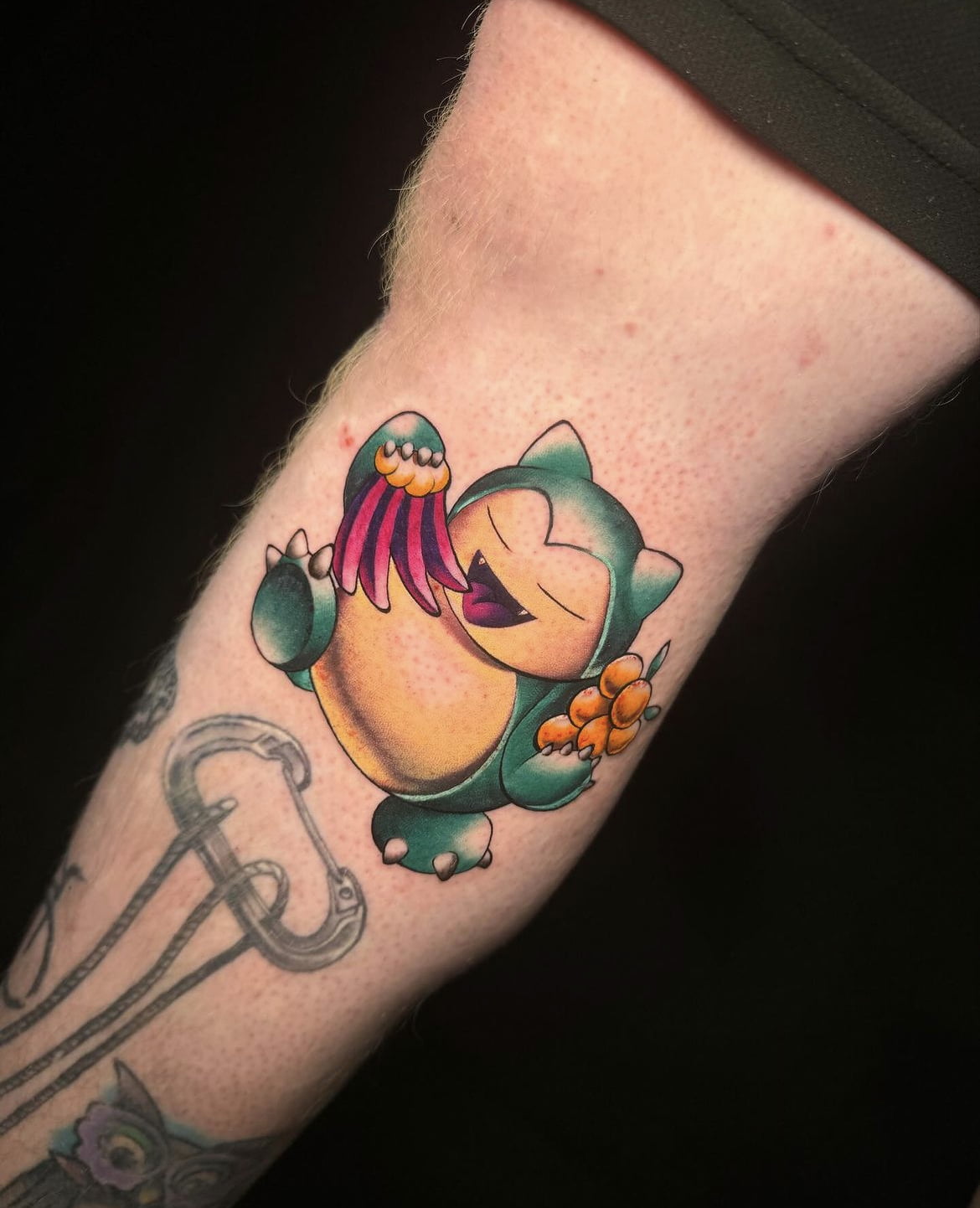 Tatuaje vibrante de Snorlax comiendo, estilo color, en la pierna.