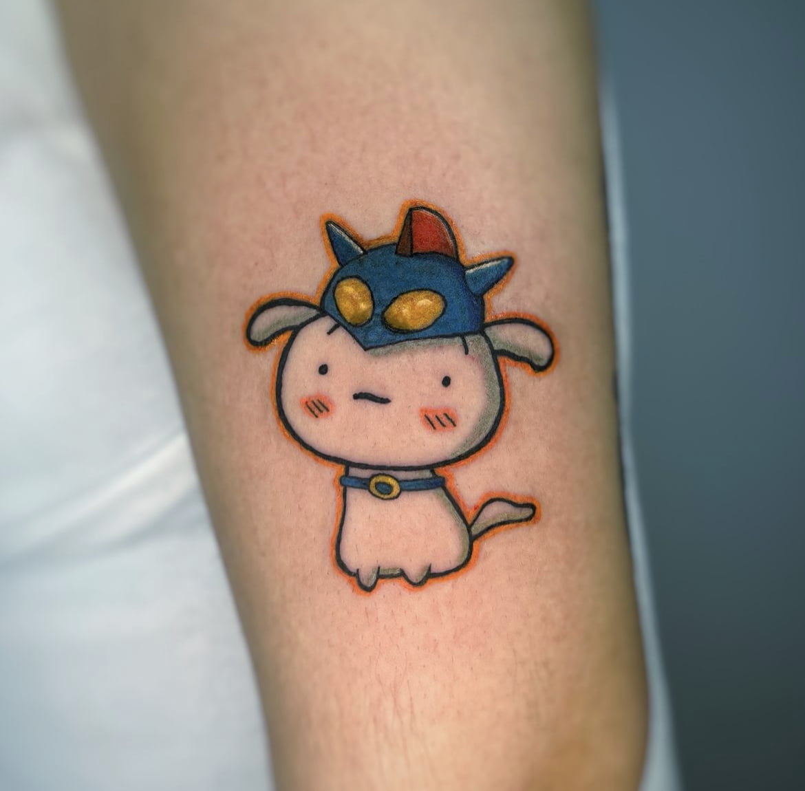 Tatuaje estilo kawaii de personaje adorable con casco azul en el brazo, colores suaves y líneas finas.