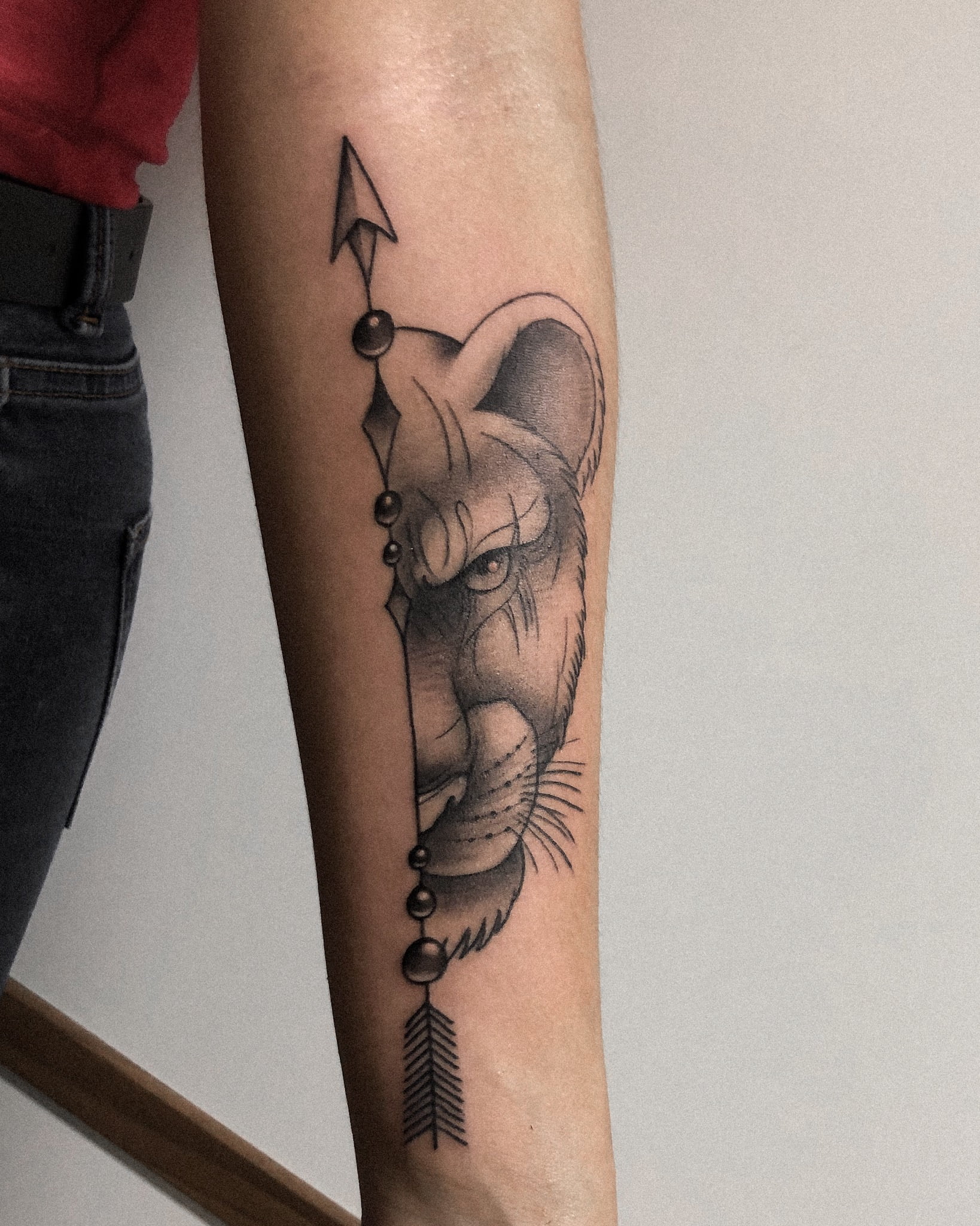 Tatuaje de leona con estilo fineline y geométrico en el antebrazo, transmitiendo fuerza y elegancia.