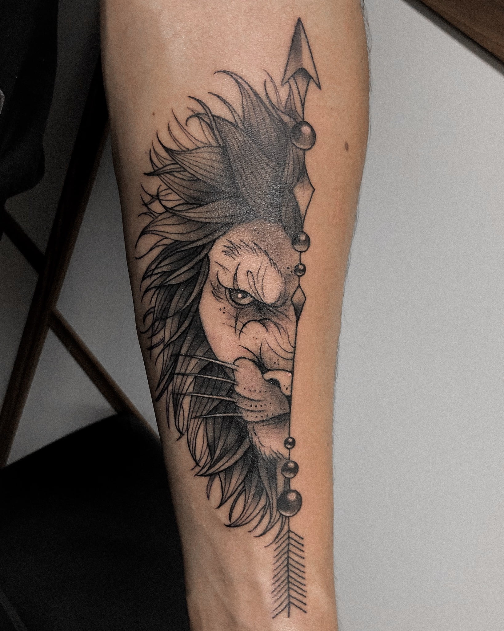 Tatuaje de medio rostro de león en estilo blackwork, con detalles de flecha, sobre el brazo, transmitiendo fuerza.