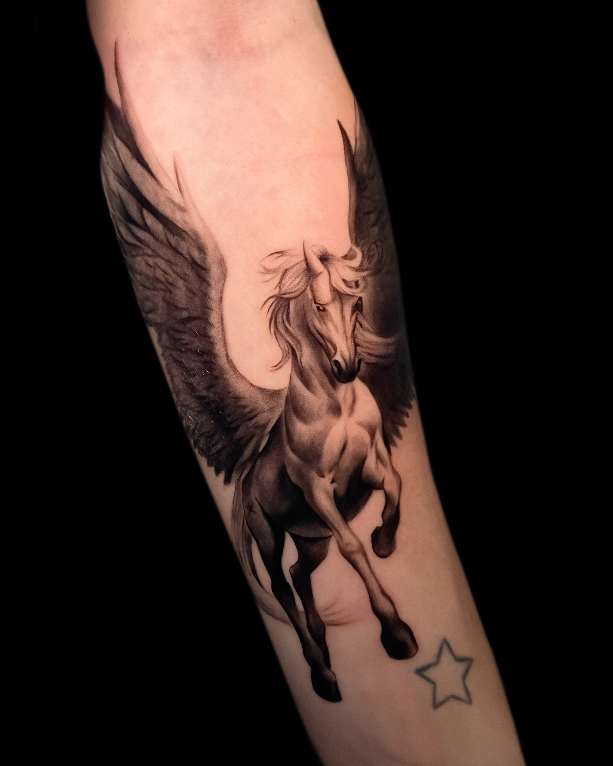 Tatuaje de un Pegaso en estilo black and grey en el antebrazo, transmitiendo libertad