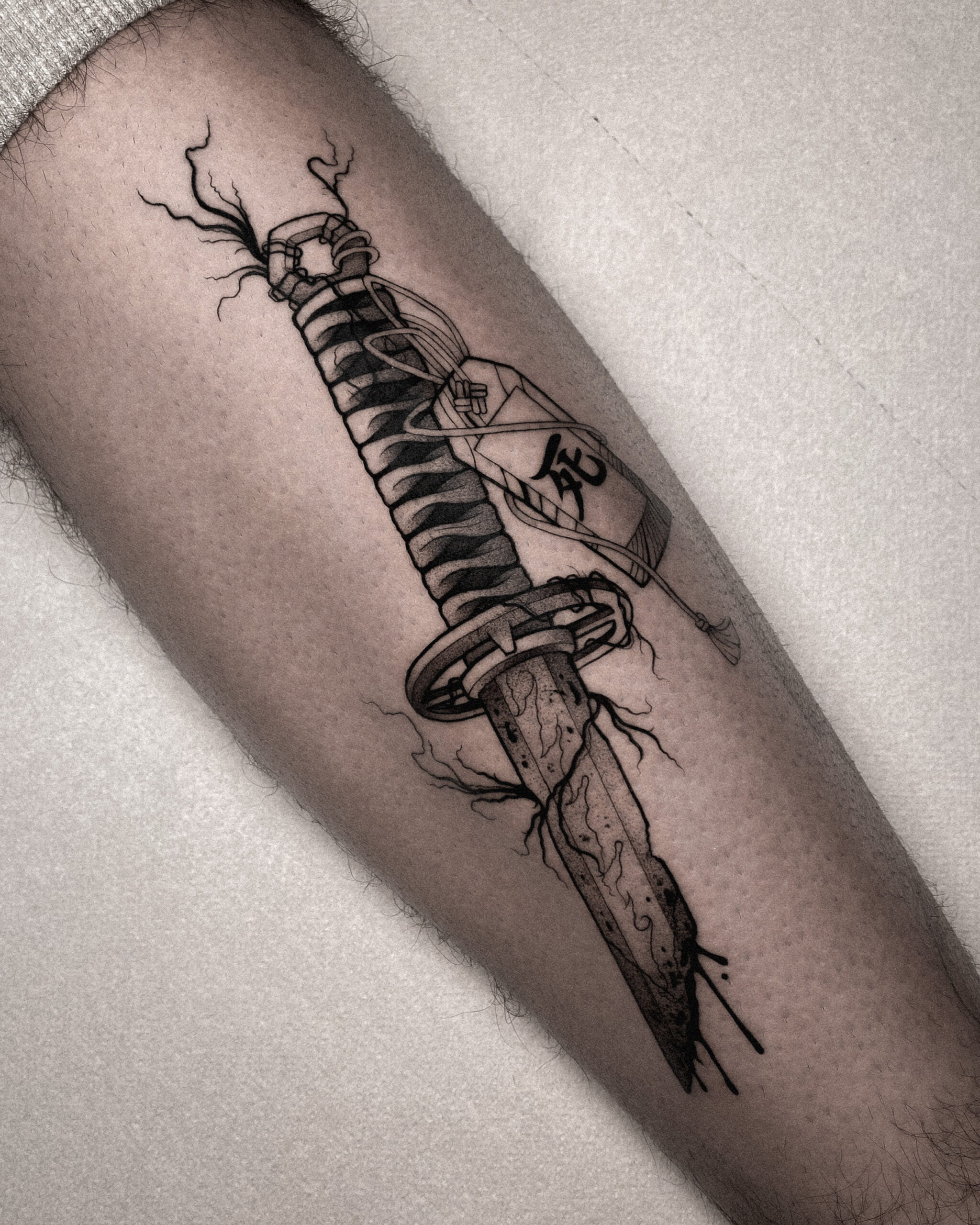 Tatuaje blackwork de una katana clavada en la pierna.