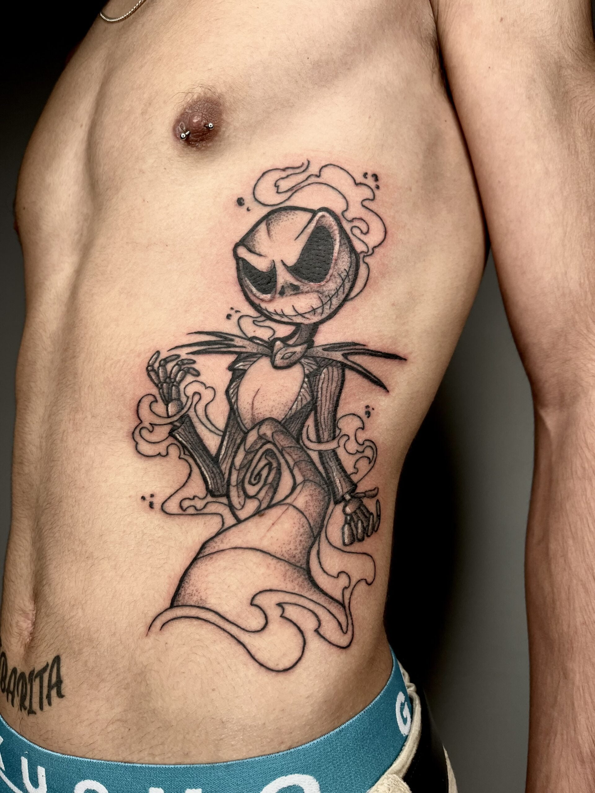 Tatuaje de Jack Skellington en estilo blackwork en el costado, transmitiendo tenebrosidad con líneas definidas y sombreado suave.