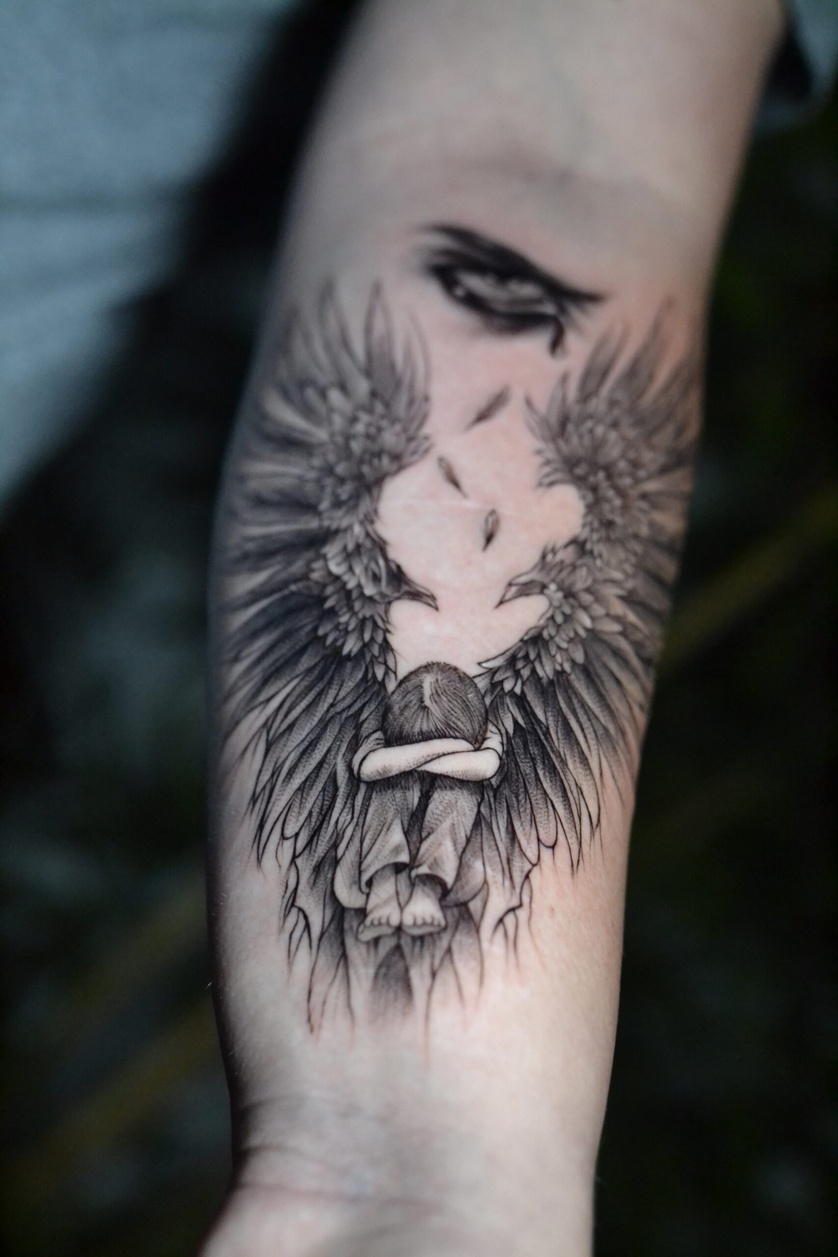 Tatuaje de un ángel triste con alas detalladas en estilo black and grey en el antebrazo.