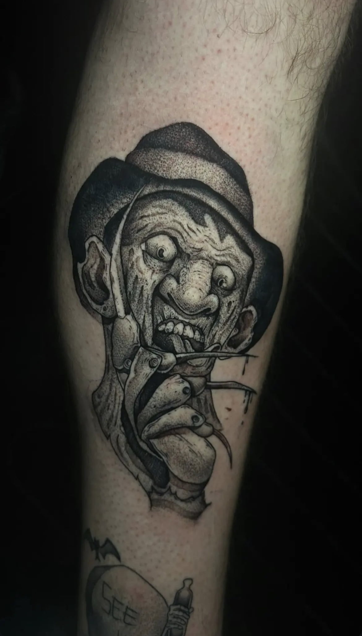 Tatuaje de personaje de terror en estilo blackwork con sombrero en la pierna, transmitiendo inquietud.