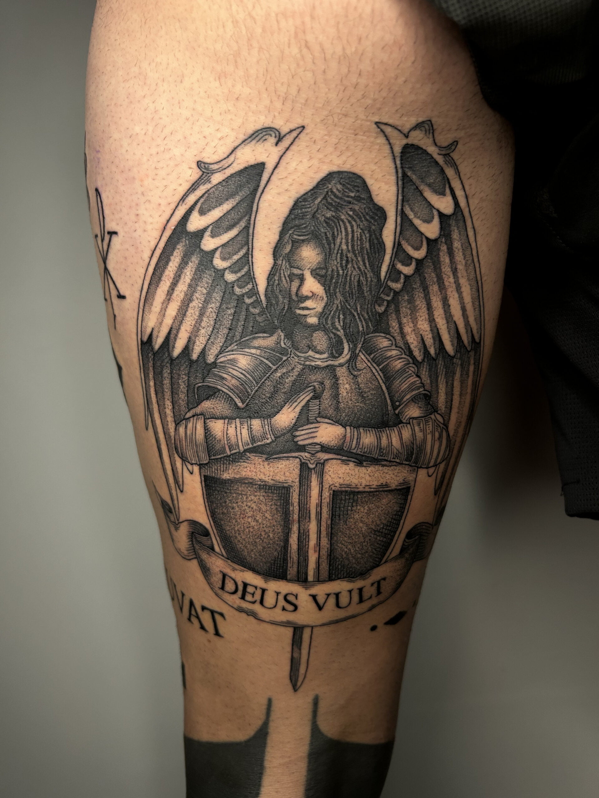 Tatuaje de un ángel guerrero con armadura en estilo black and grey, en el muslo, transmitiendo fuerza y determinación.