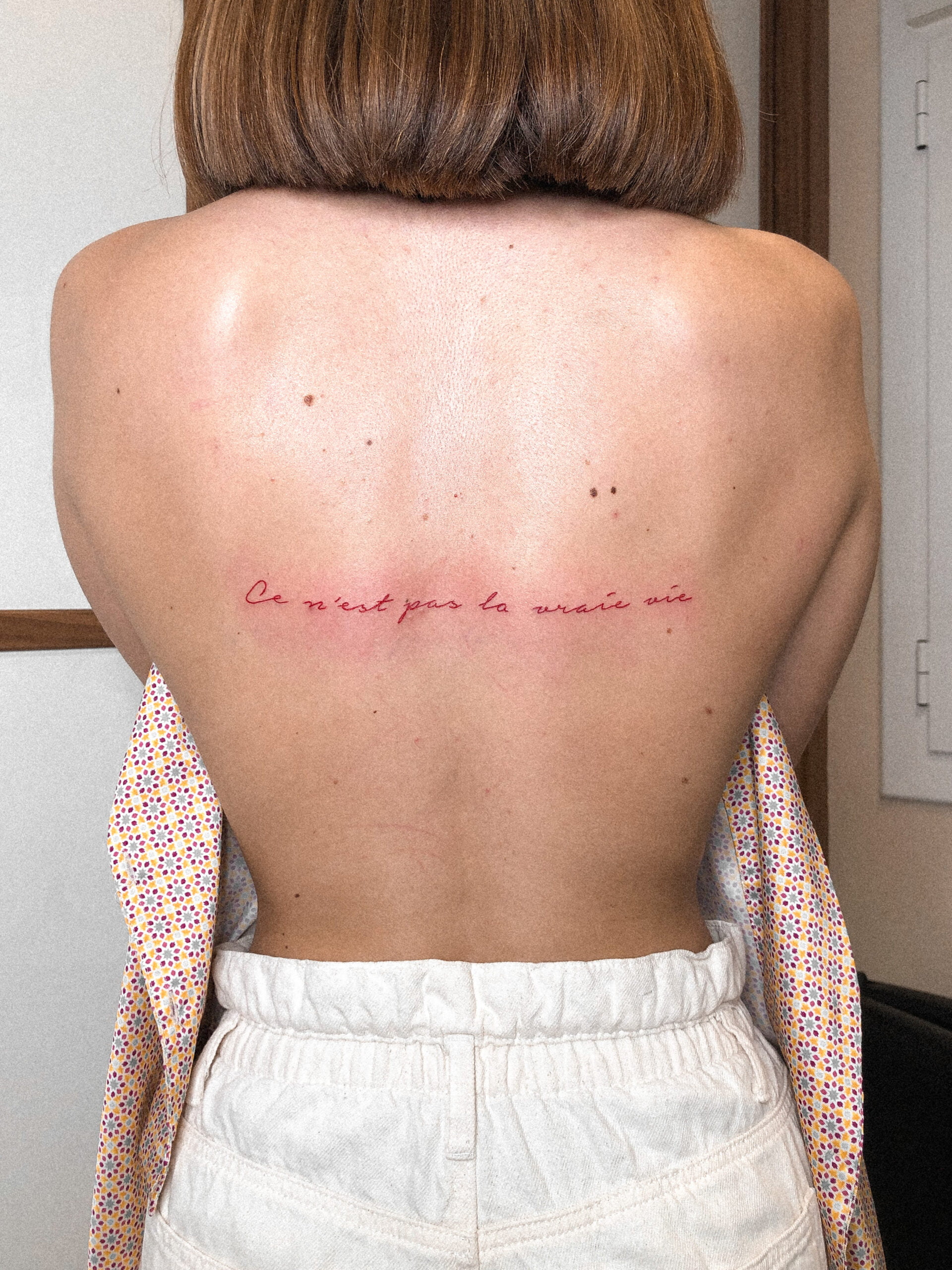 Tatuaje de texto en estilo fineline con frase en la espalda, evocando introspección.