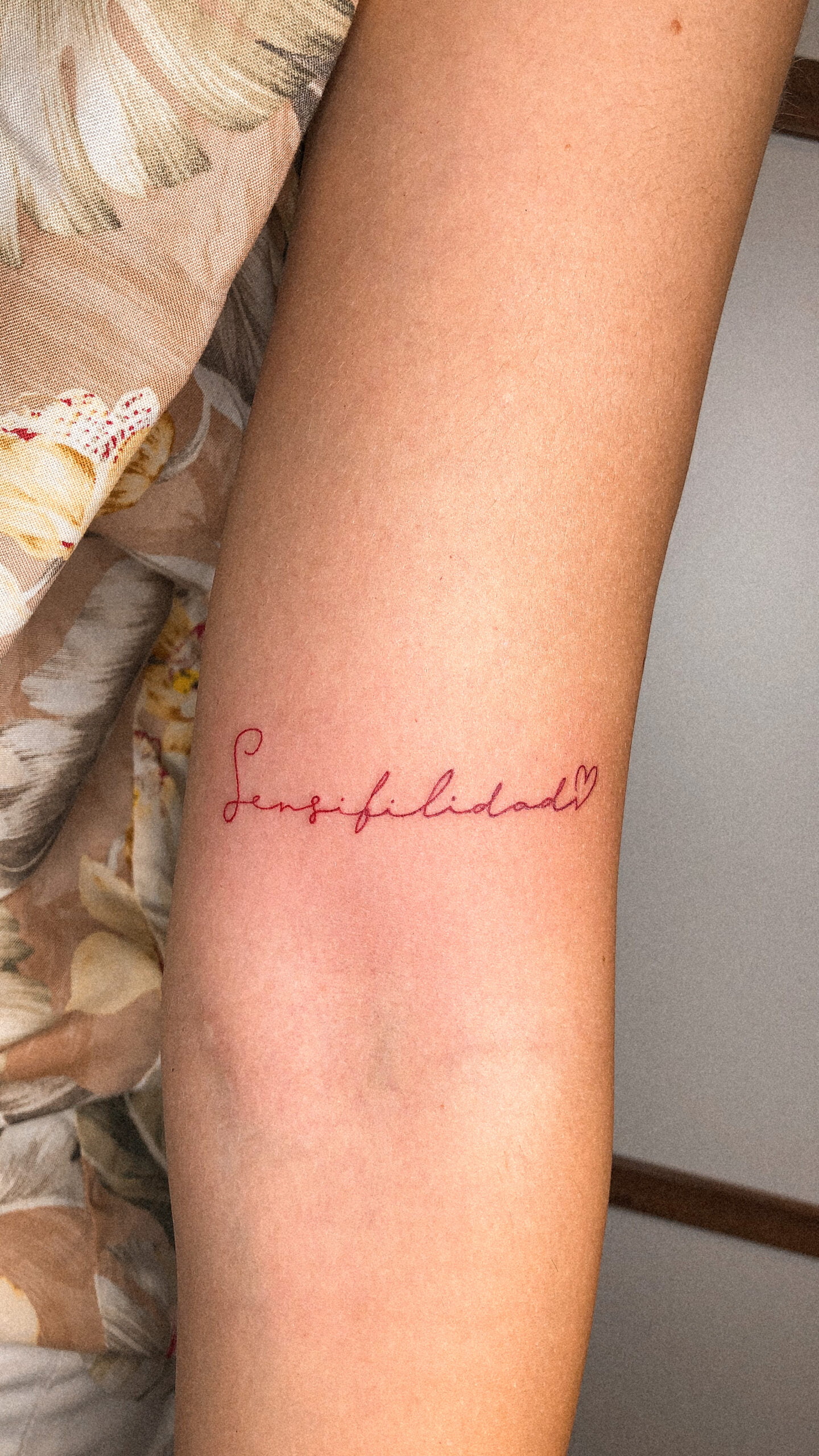 Tatuaje minimalista con la palabra 'Sensibilidad' y un corazón en el antebrazo.