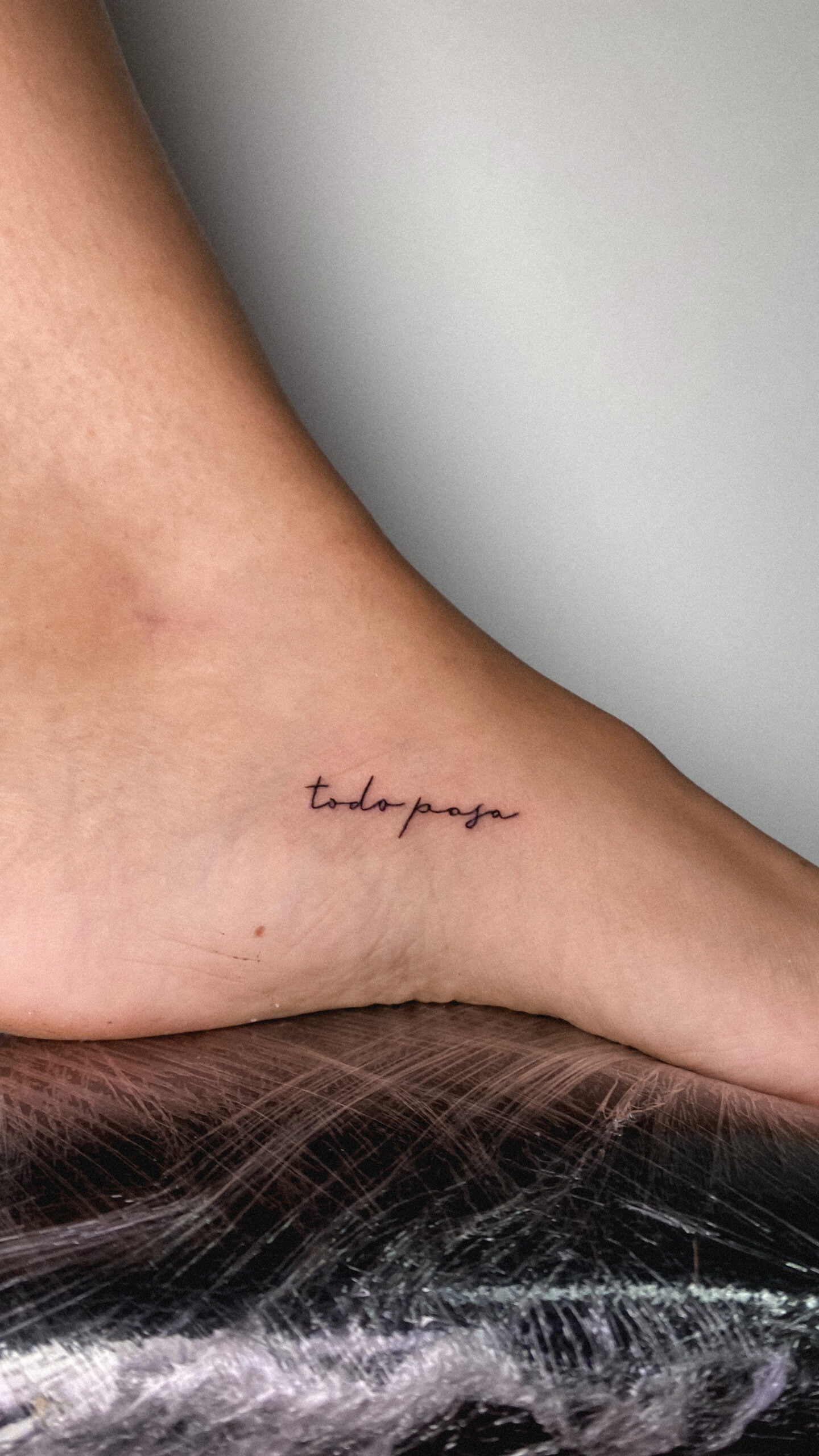 Tatuaje de frase 'todo pasa' en estilo fineline en el pie, transmitiendo serenidad.