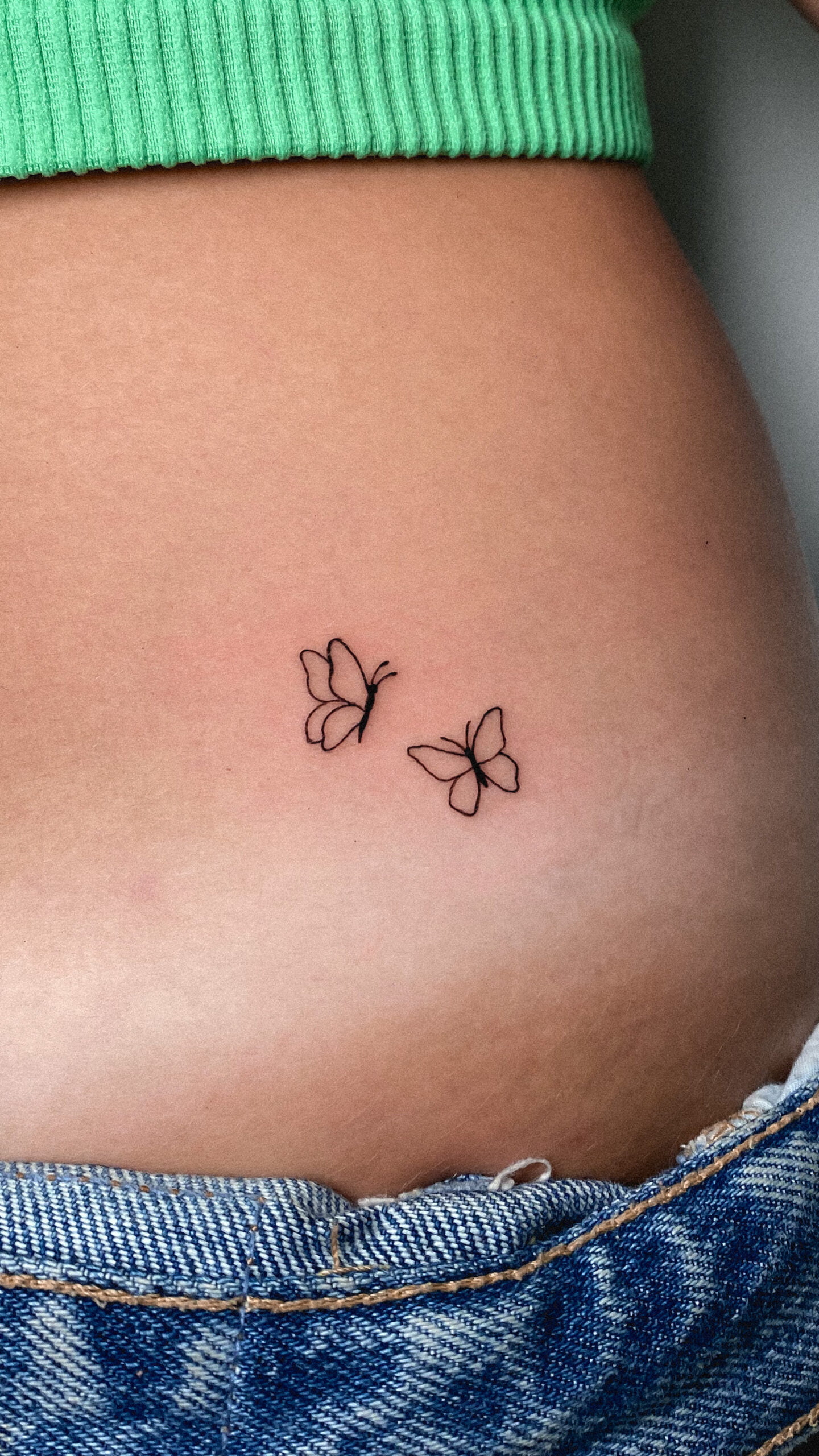 Tatuaje minimalista de dos mariposas en fineline en la cadera que transmite libertad.