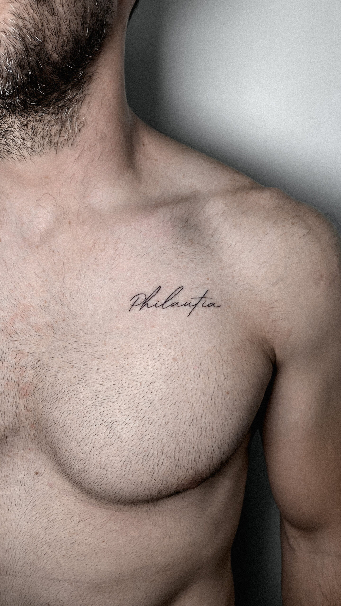Tatuaje de la palabra 'Philautia' en estilo minimalista en el pecho.