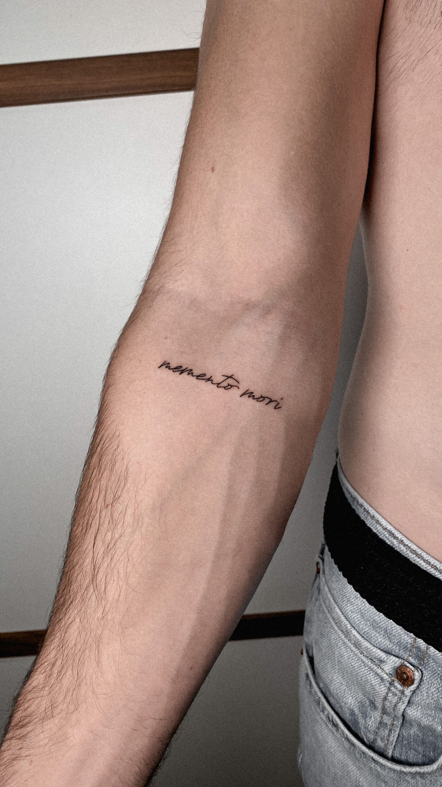 Tatuaje de frase 'memento mori' en estilo fineline en el antebrazo.