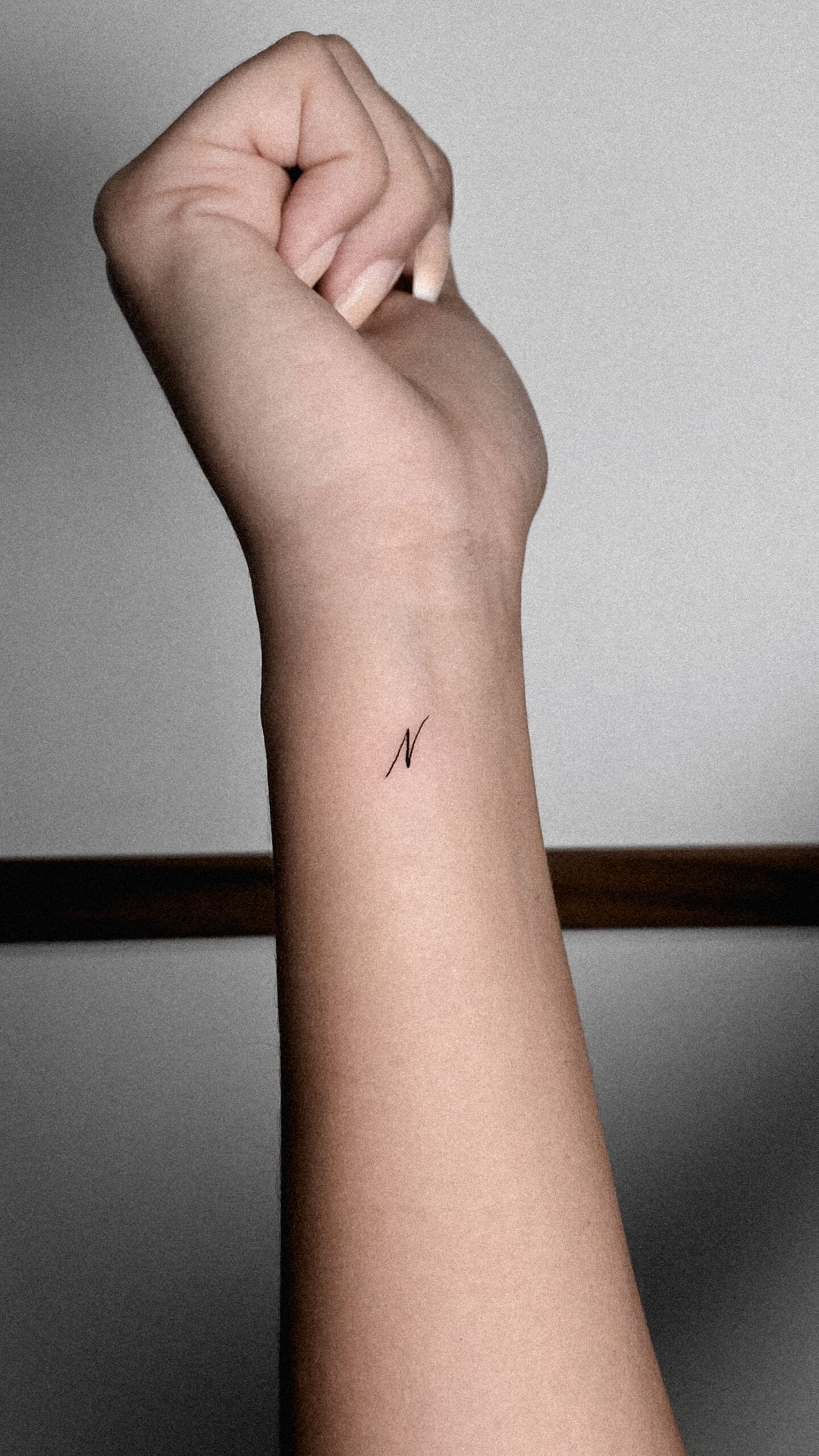 Tatuaje minimalista de letra N en estilo fineline en la muñeca.