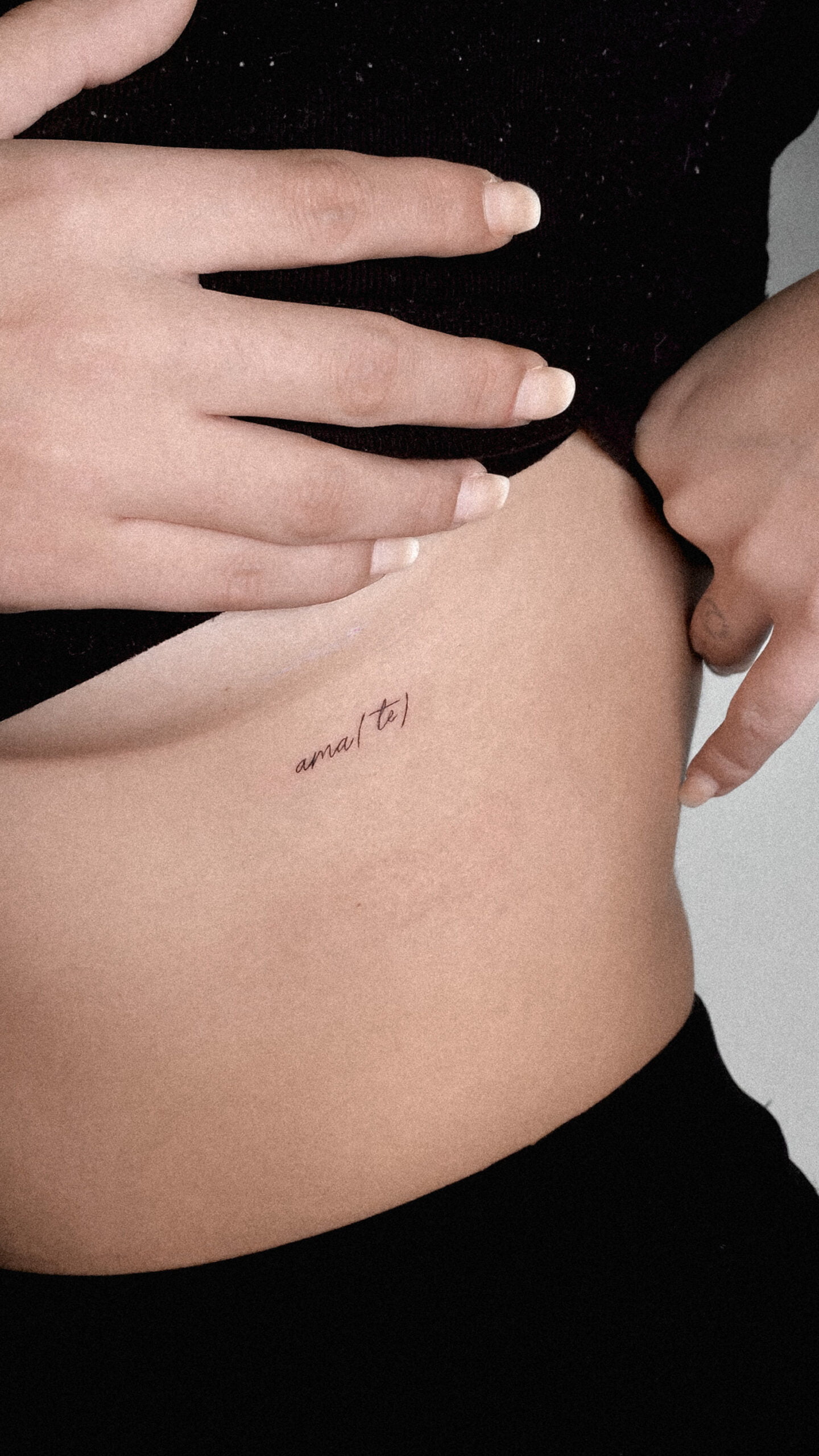 Tatuaje de texto 'amar(te)' en estilo fineline en el abdomen.