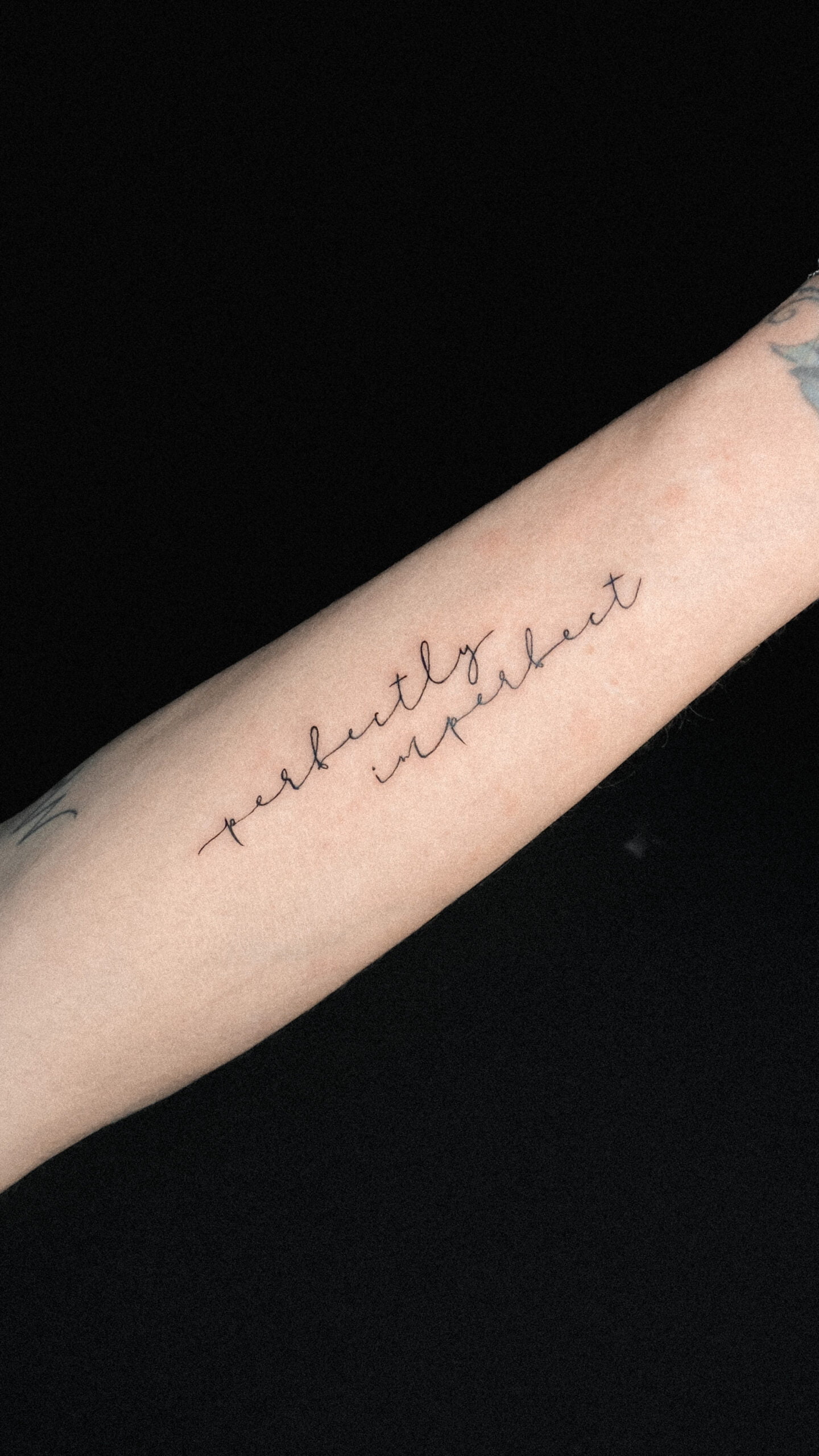 Tatuaje de frase 'perfectly imperfect' en estilo Fineline en el antebrazo.