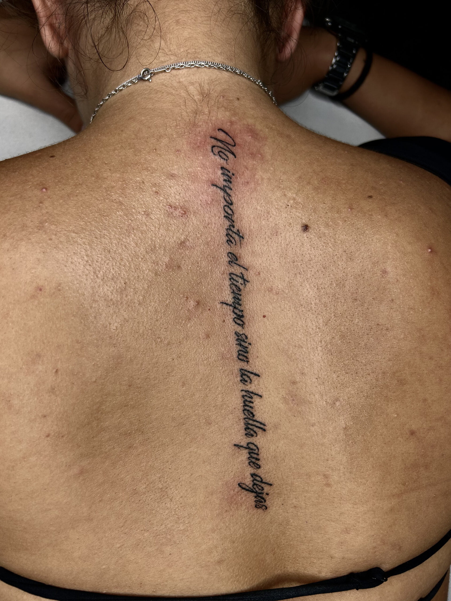 Tatuaje de frase cursiva en la espalda con estilo minimalista y toque emocional.