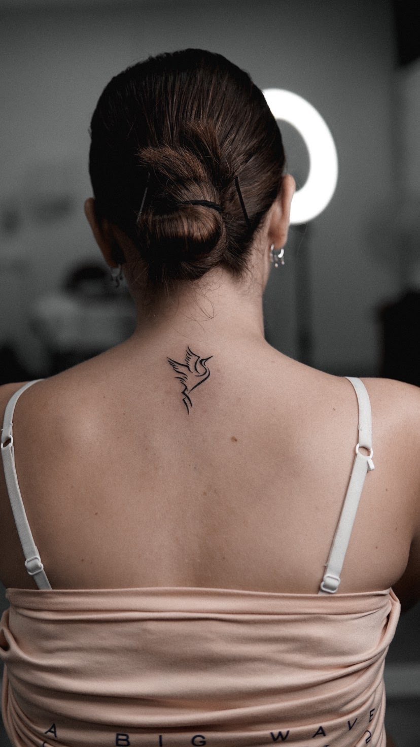 Tatuaje de un ave estilizada en estilo minimalista sobre la nuca de una mujer.