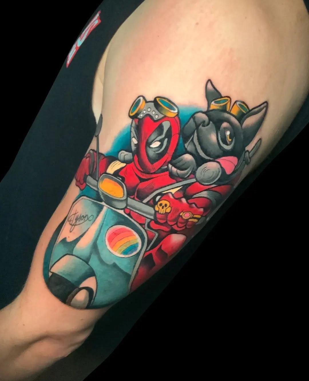 Tatuaje en estilo neotradicional de Deadpool y un perro en motocicleta, en el brazo, con colores vibrantes y estilo cómico.