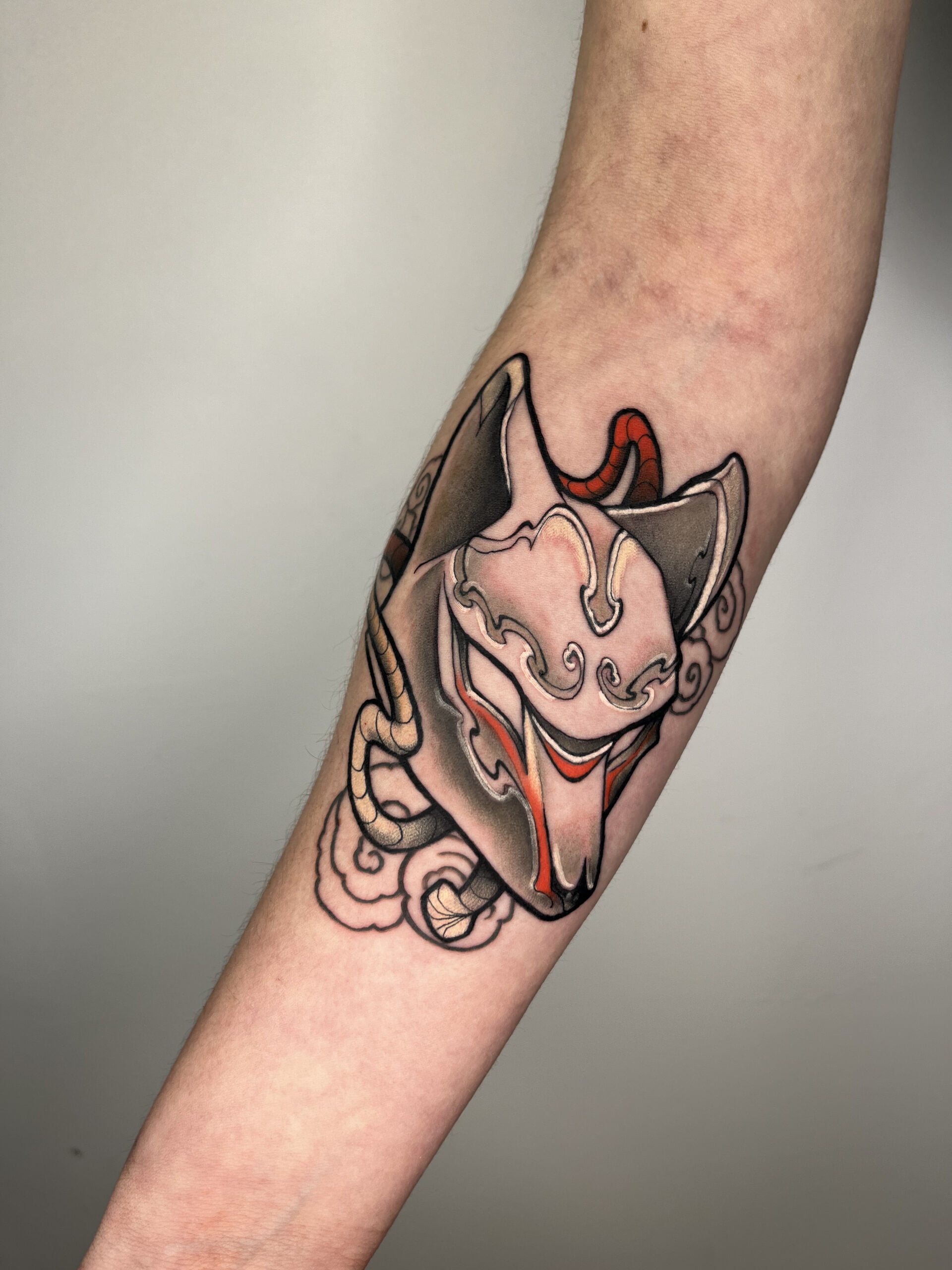 Tatuaje de máscara kitsune estilo neotradicional en antebrazo, con detalles en negro y rojo.