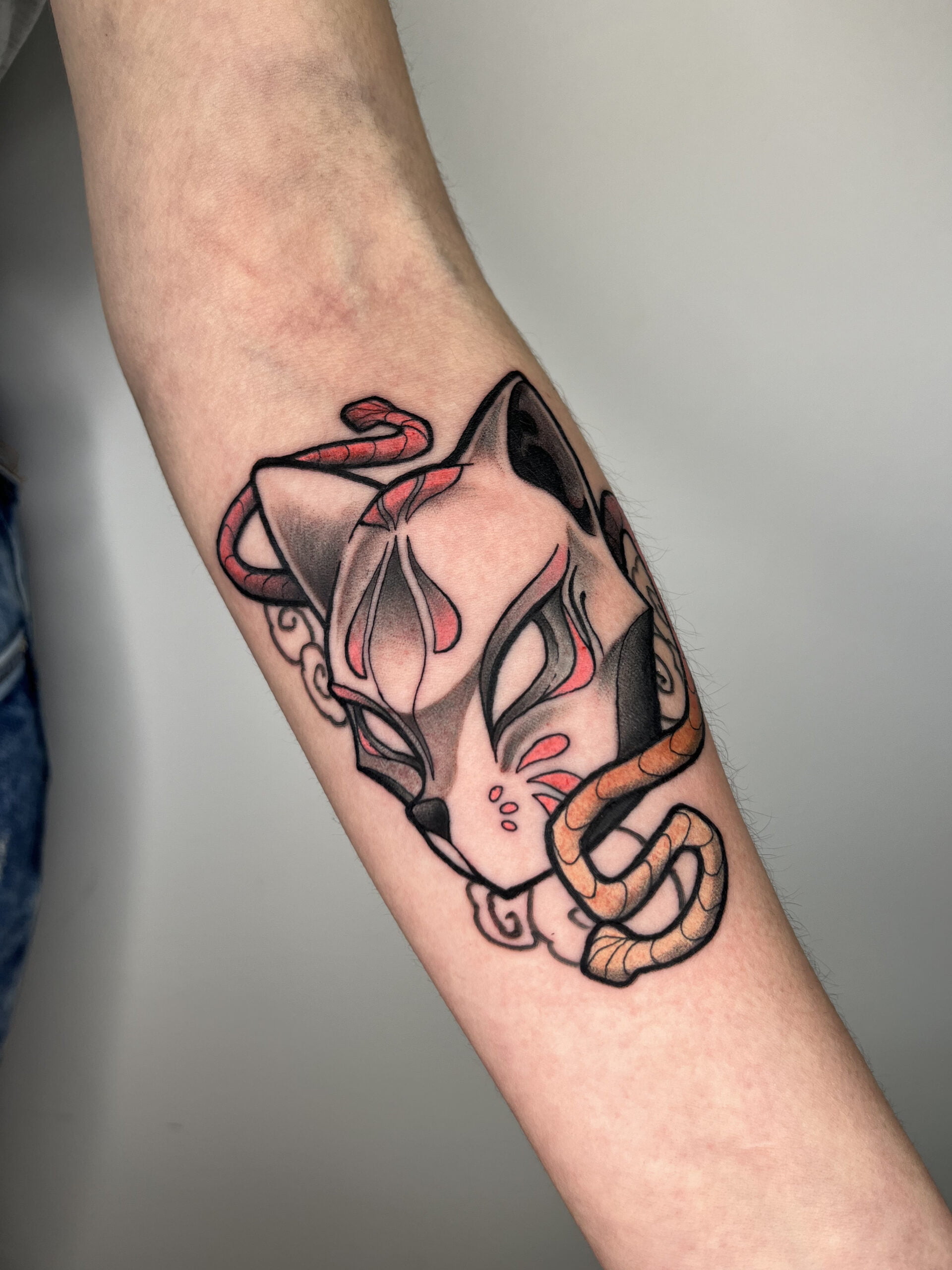 Tatuaje de máscara de kitsune en estilo neotradicional en el brazo, con líneas audaces y detalles coloridos, transmitiendo misticismo.