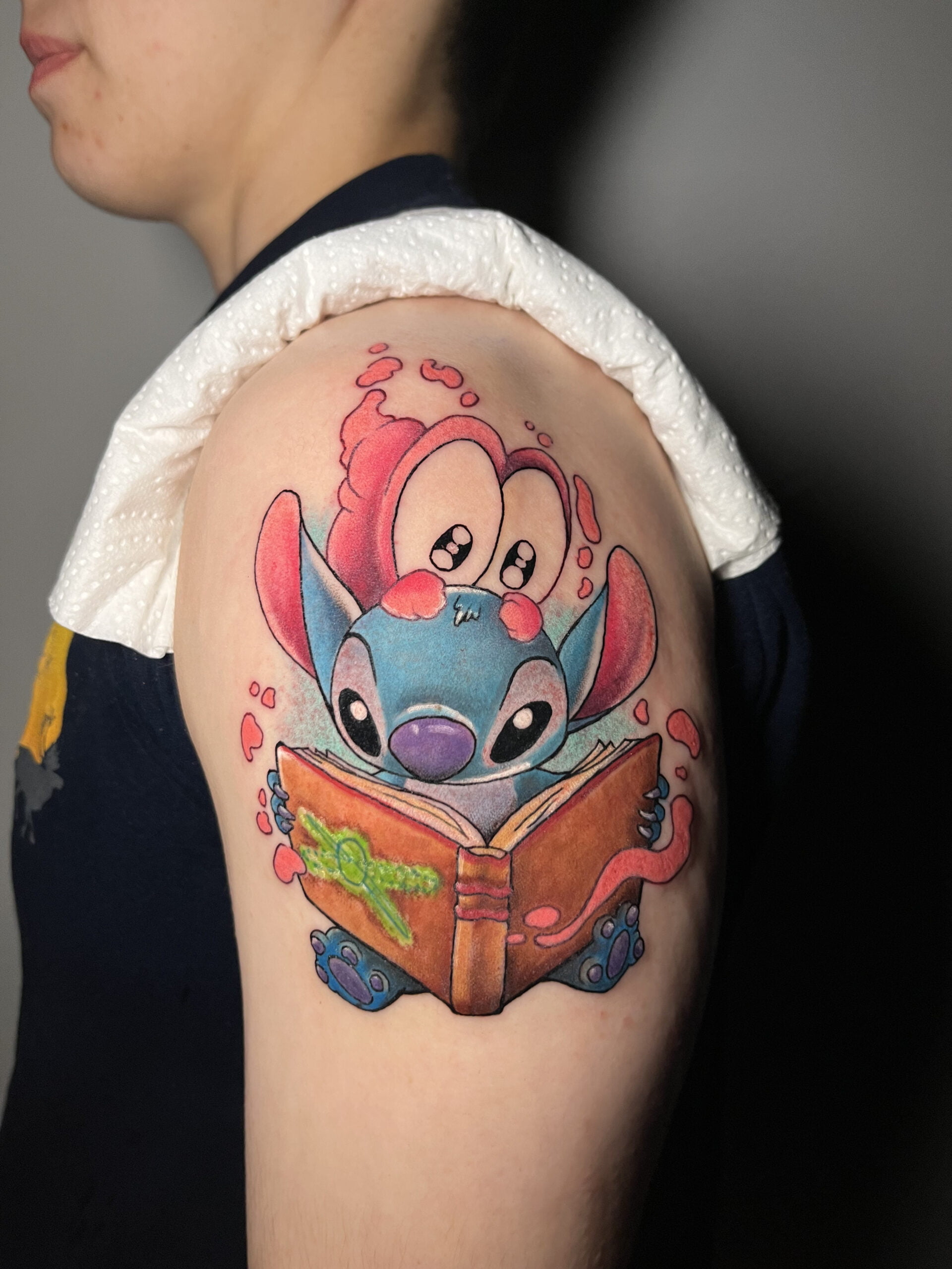 Tatuaje de Stitch leyendo un libro, estilo neotradicional en el brazo.