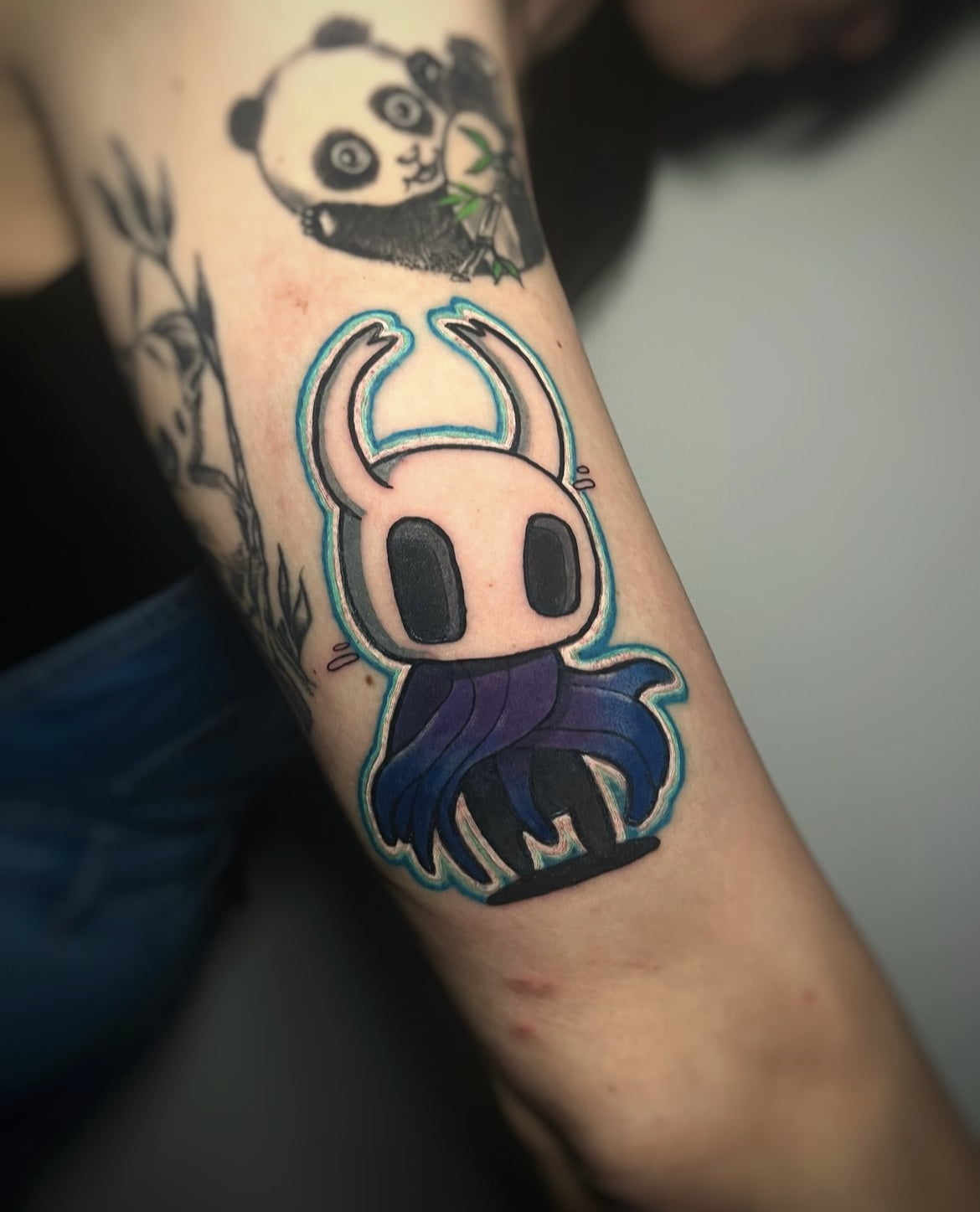 Tatuaje de personaje Hollow Knight en estilo kawaii con colores vivos en brazo.