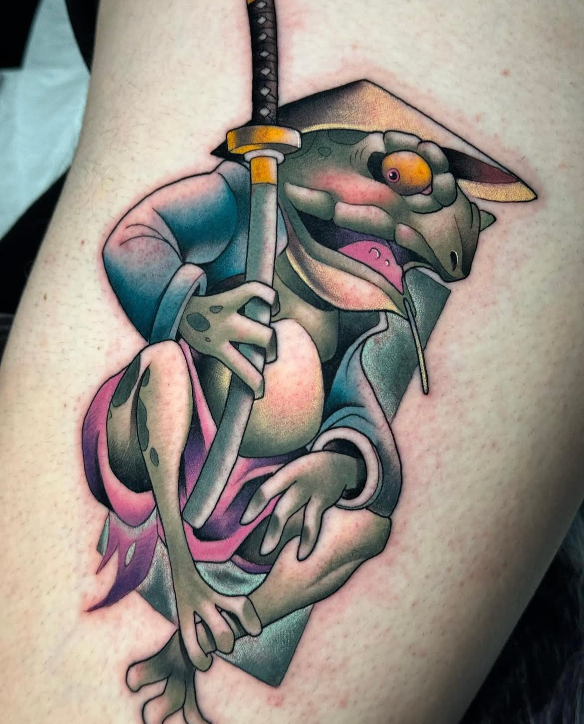 Tatuaje de rana samurái con estilo neotradicional en muslo, técnica de colores vibrantes y detalles finos.