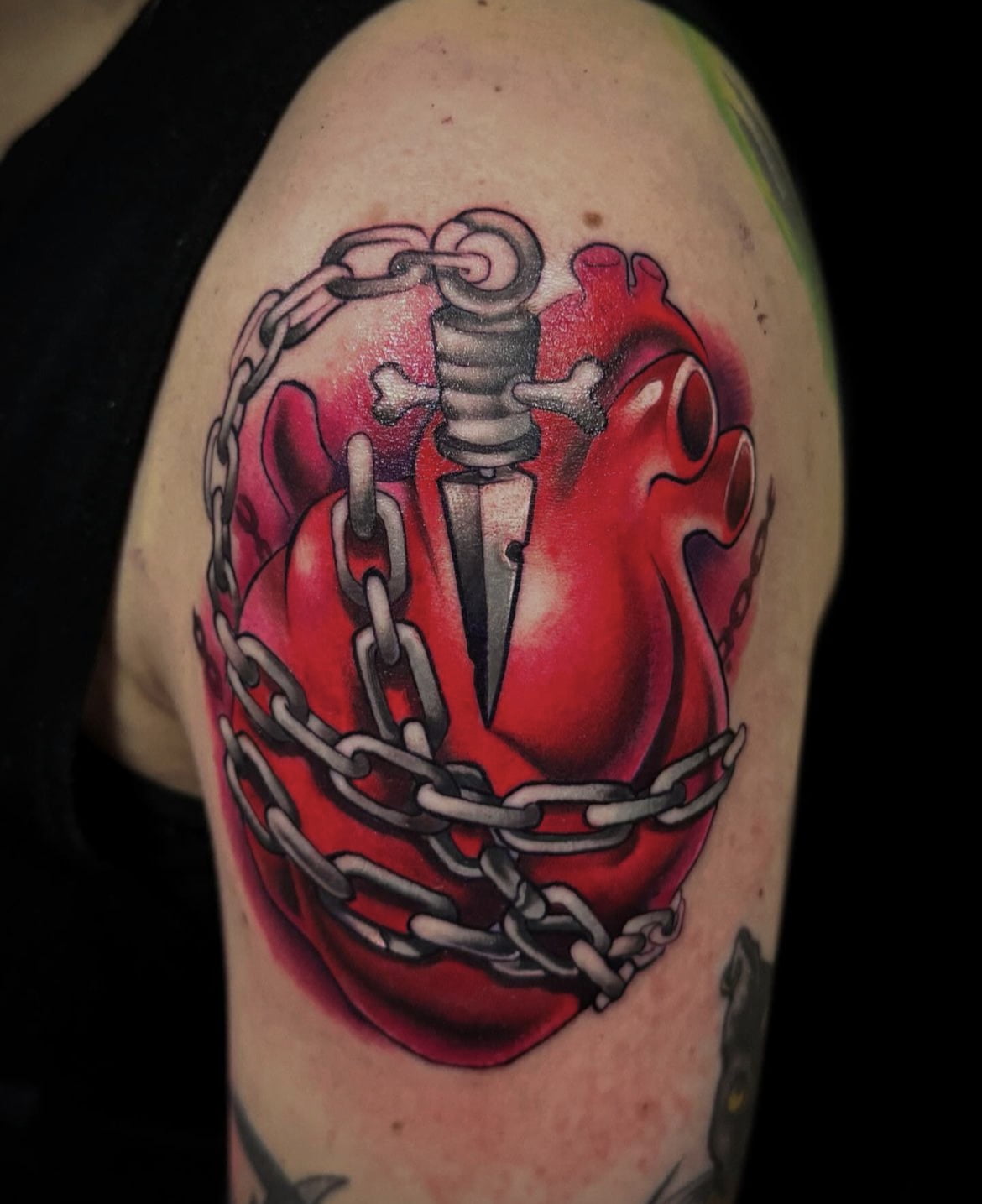 Corazón estilo neotradicional con daga y cadenas en el brazo, técnica en colores vivos.