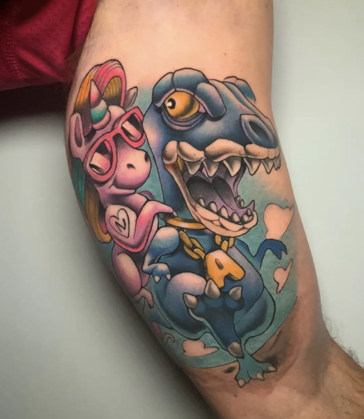 Tatuaje colorido de un unicornio y un dinosaurio en estilo neotradicional, ubicado en el brazo, transmitiendo diversión y fantasía.