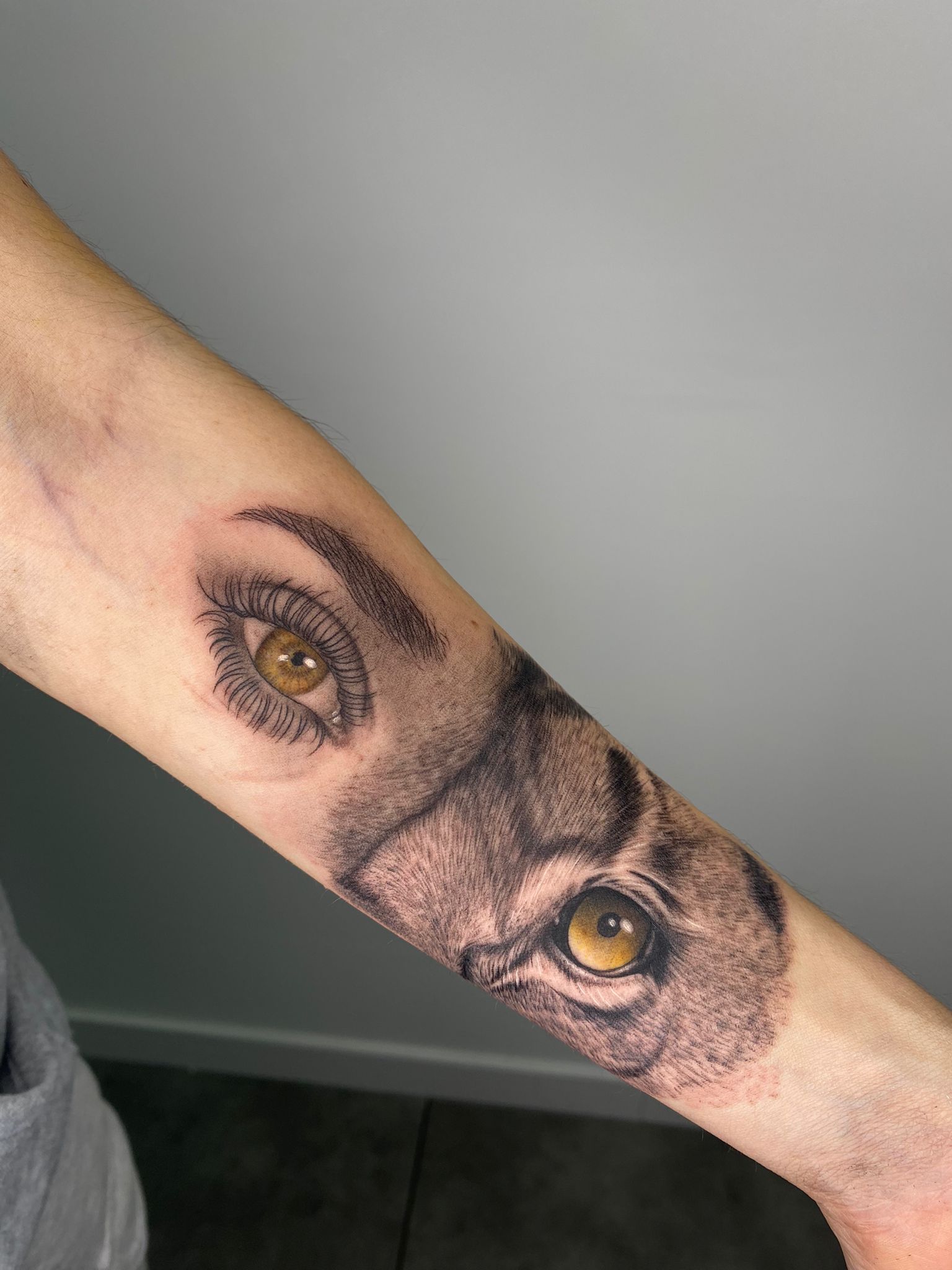 Tatuaje realista de ojos humano y lobo en black and grey en antebrazo, transmitiendo conexión y dualidad.
